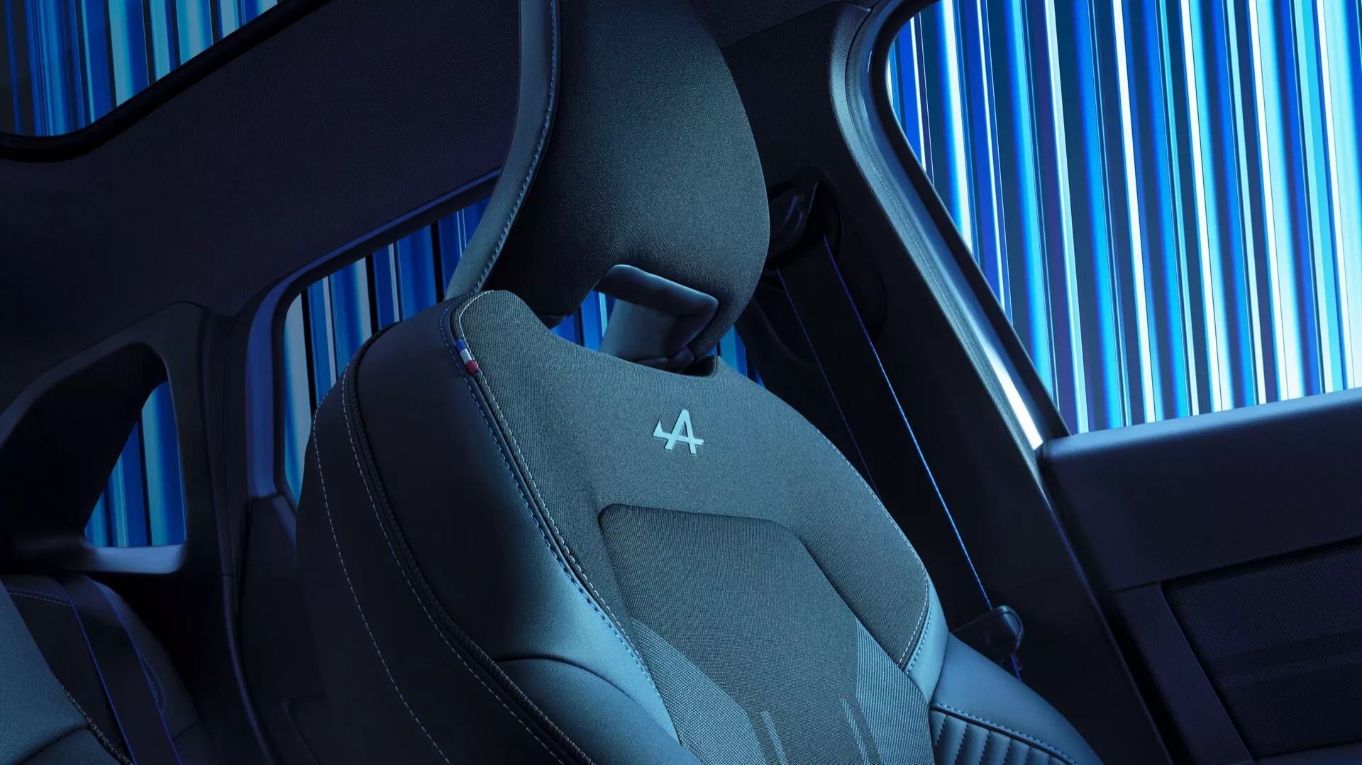 Zbliżony widok wnętrza fotela pojazdu Renault Symbioz 2024 pierwszej generacji, podkreślający cechy nowoczesnego designu i technologii. Ukazuje górną część fotela o ergonomicznym kształcie, profilowane boczne podparcia oraz połączenie skóry i oddychającej tkaniny dla luksusu i wygody. Zauważalne czerwone przeszycia na zagłówku z wytłoczonym logo, wraz z widocznym wzorem bocznej szyby samochodu i eleganckim designem kabiny.