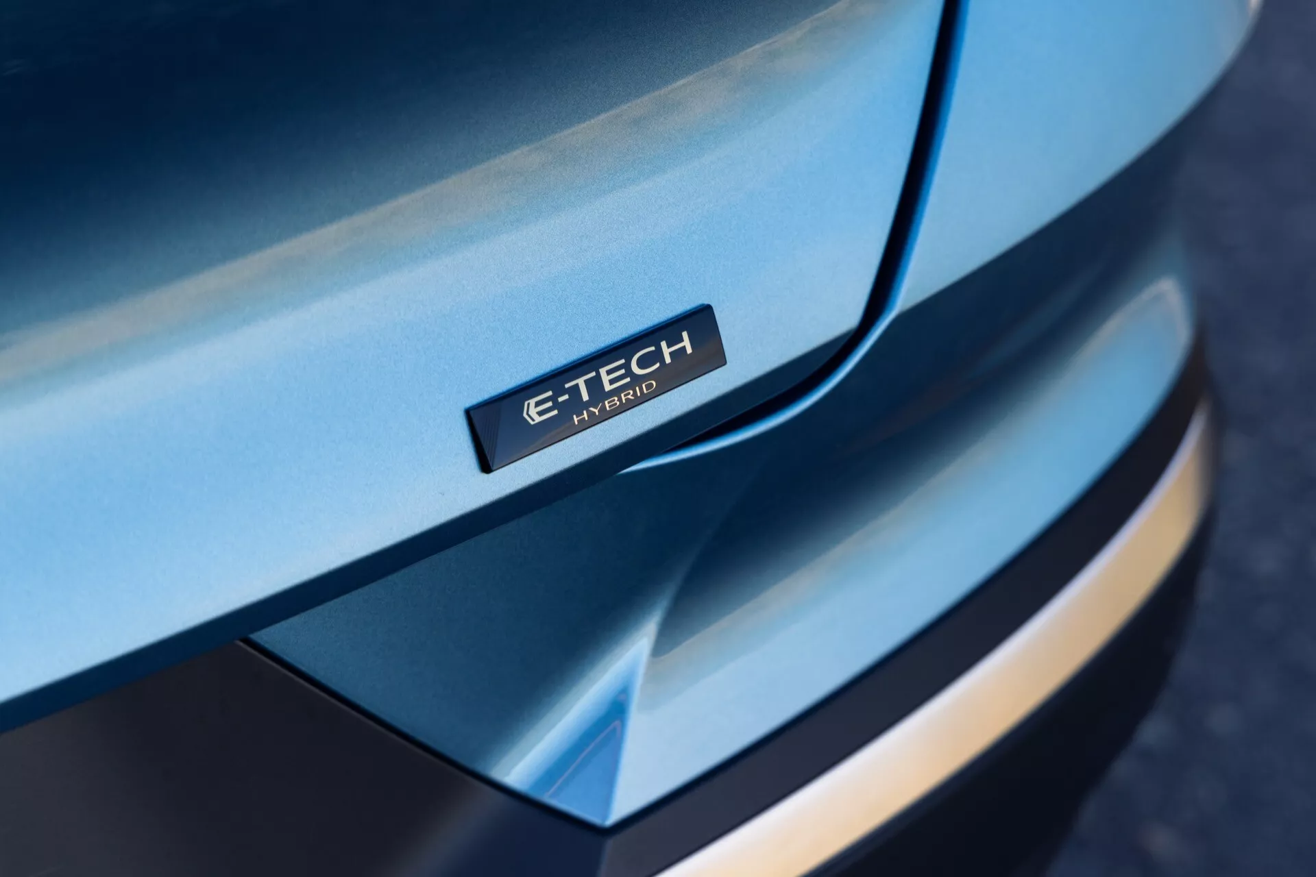 Zbliżony widok pod kątem na przednią część Renault Symbioz 2024, koncentrujący się na smukłej, zakrzywionej masce z odznaką 'E-TECH Hybrid', wielowarstwowym projektem przedniego zderzaka, kontrastującymi kolorami i premium wyglądem, podkreślając technologię hybrydową.