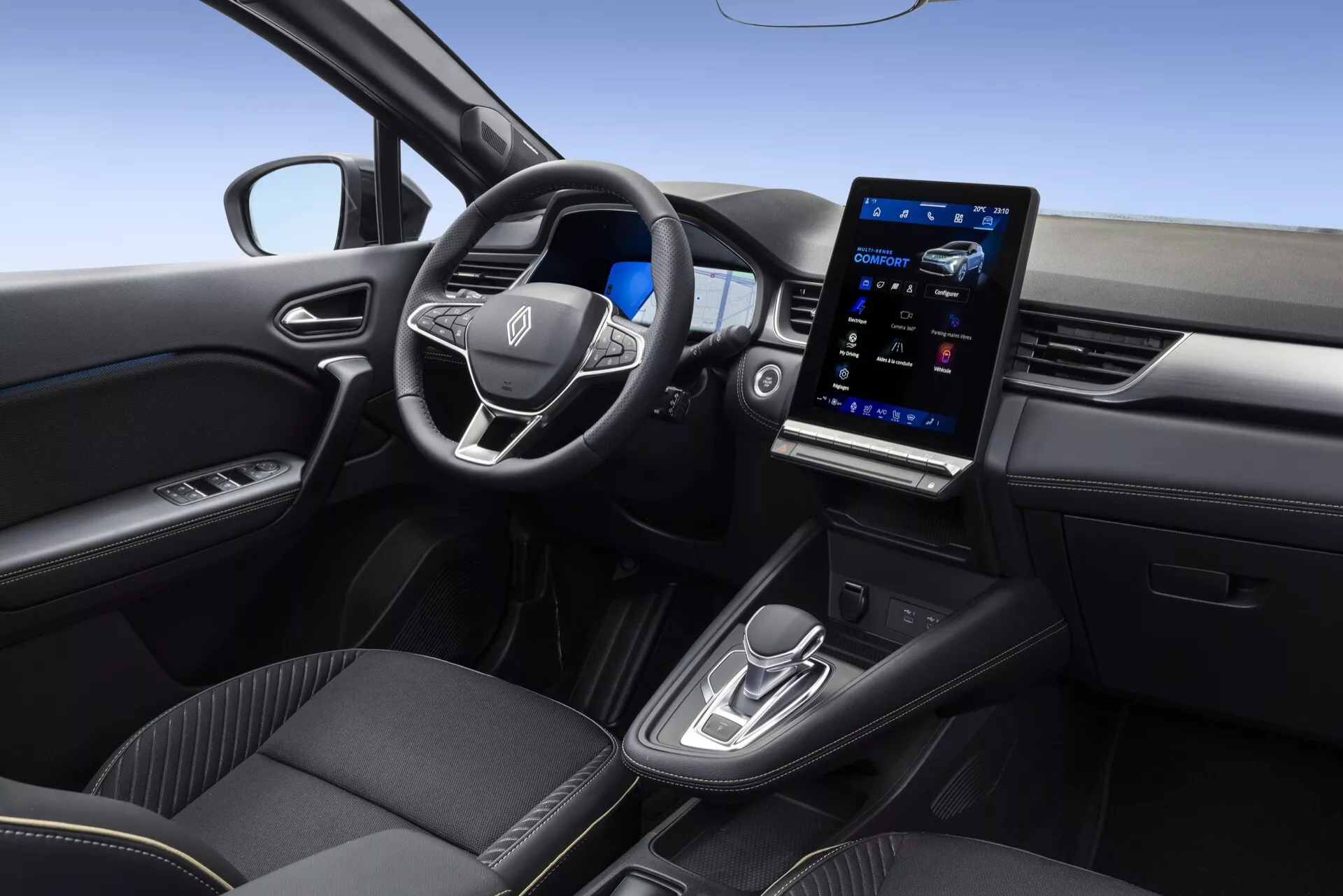 Wnętrze Renault Symbioz 2024, skoncentrowane na stronie kierowcy, widziane z podwyższonego kąta około 45 stopni. Wyposażone w trójramienną kierownicę z wbudowanymi przyciskami sterującymi do audio, zestawu głośnomówiącego i tempomatu. Duży, pionowo zorientowany system infotainment z ekranem dotykowym dominuje w centrum deski rozdzielczej, pokazując zaawansowane funkcje łączności. Poniżej ekranu znajdują się minimalistyczne przyciski dwustrefowej klimatyzacji. Konsola centralna zawiera ergonomiczny automatyczny lewarek zmiany biegów i selektor trybu jazdy. Wykończenia tapicerki premium i sterowniki w drzwiach do elektrycznych szyb i lusterek bocznych poprawiają komfort i styl.