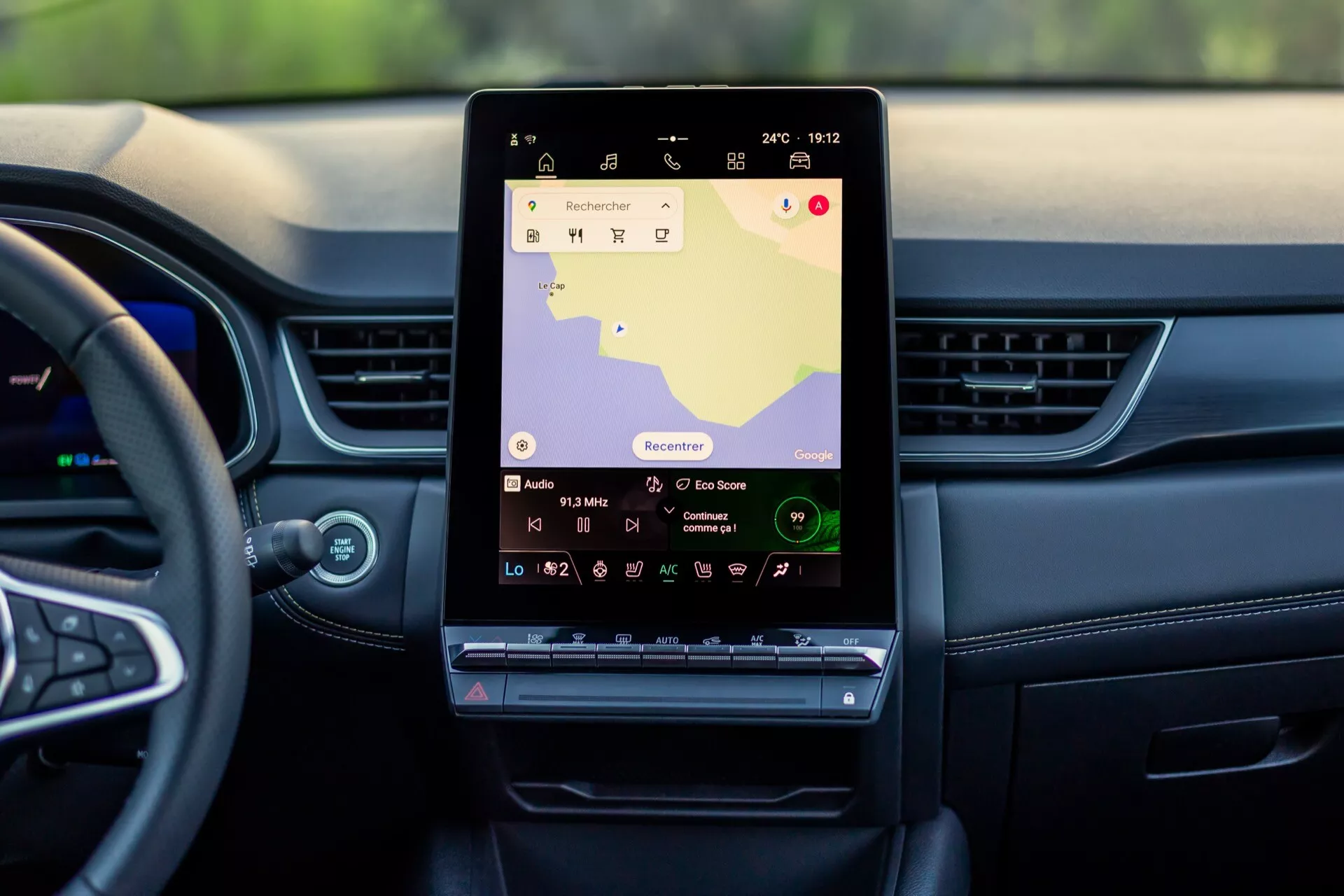 Widok wnętrza Renault Symbioz 2024 (1. generacja) z perspektywy tylnego siedzenia, pokazujący duży pionowy ekran dotykowy na konsoli środkowej z mapą nawigacyjną i kontrolkami multimedialnymi; nowoczesna deska rozdzielcza z poziomymi liniami i wentylatorami, częściowo widoczną kierownicą, podkreślając zaawansowany system infotainment i funkcje high-tech.