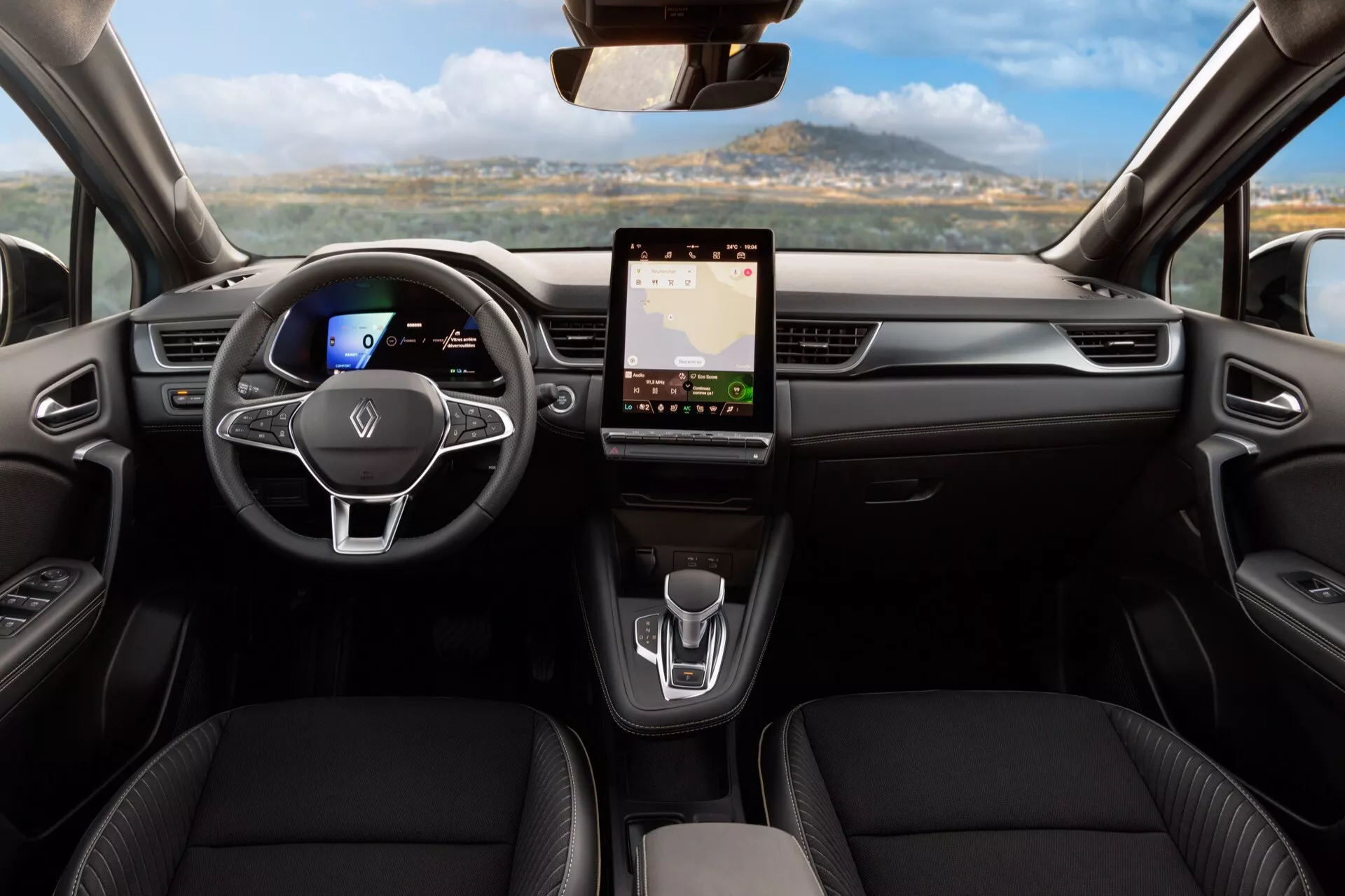 Wnętrze Renault Symbioz 2024 pierwszej generacji z perspektywy tylnego siedzenia, pokazujące deskę rozdzielczą i obszar przednich siedzeń. Posiada centralnie umieszczoną kierownicę z płaskim dnem i wielofunkcyjnymi kontrolkami, cyfrowy zestaw wskaźników, duży system informacyjno-rozrywkowy z ekranem dotykowym, minimalistyczne sterowanie klimatyzacją, nowoczesny selektor biegów i konturowane siedzenia z materiału przypominającego skórę, podkreślające nowoczesny design i zaawansowaną technologię.