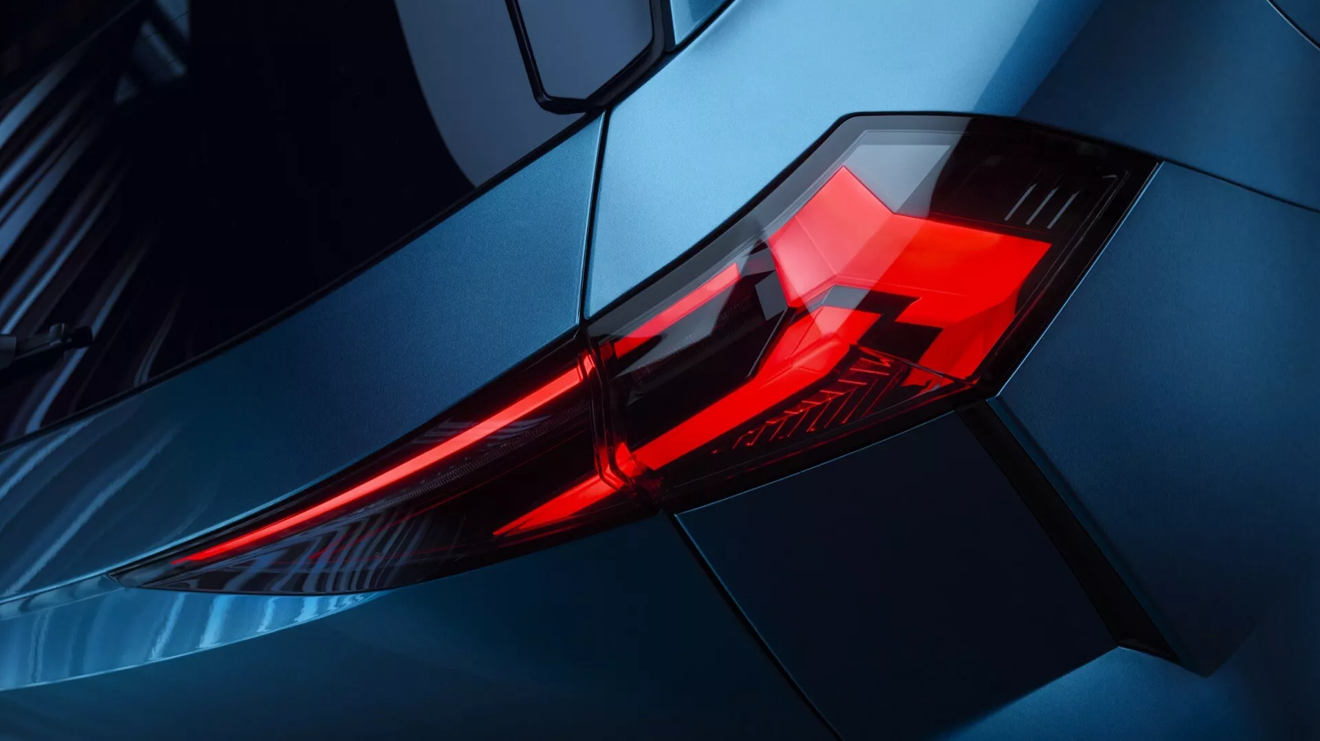 Zbliżenie tylnego światła Renault Symbioz 2024, prezentujące elementy oświetlenia LED w kątowej, warstwowej obudowie. Zdjęcie wykonane pod ukośnym kątem, skupiające się na lewym tylnym rogu z podwyższonym widokiem, podkreślające metalicznie niebieskie nadwozie samochodu i aerodynamiczne linie. Obraz podkreśla nowoczesny, sportowy design i premium wygląd pojazdu, odpowiedni do dyskusji o technologii motoryzacyjnej i trendach projektowych.