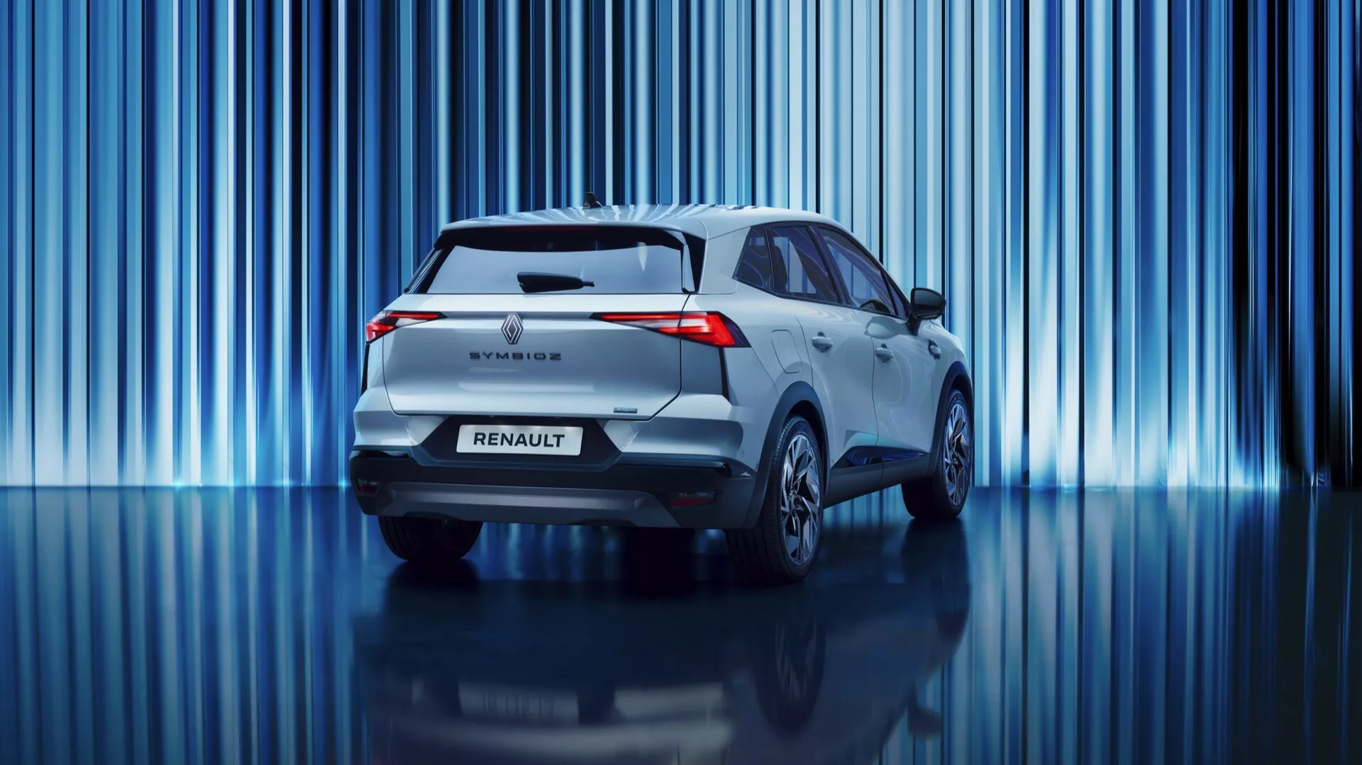 Ta profesjonalna fotografia przedstawia tylną część pierwszej generacji Renault Symbioz 2024, nowoczesnego modelu SUV. Pojazd wyposażony jest w charakterystyczne tylne światła LED, tylny spojler, tylnią wycieraczkę, znaczek Renault oraz nazwę modelu. Zdjęcie z niskiego kąta podkreśla jego sylwetkę i podkreśla czysty design bez widocznego wydechu, co sugeruje układ hybrydowy lub elektryczny. Na żywym tle z pionowymi niebieskimi smugami światła, lekki metaliczny odcień samochodu i odbijająca powierzchnia podłogi tworzą wyrafinowaną atmosferę showroomu lub inscenizowanej sesji zdjęciowej.