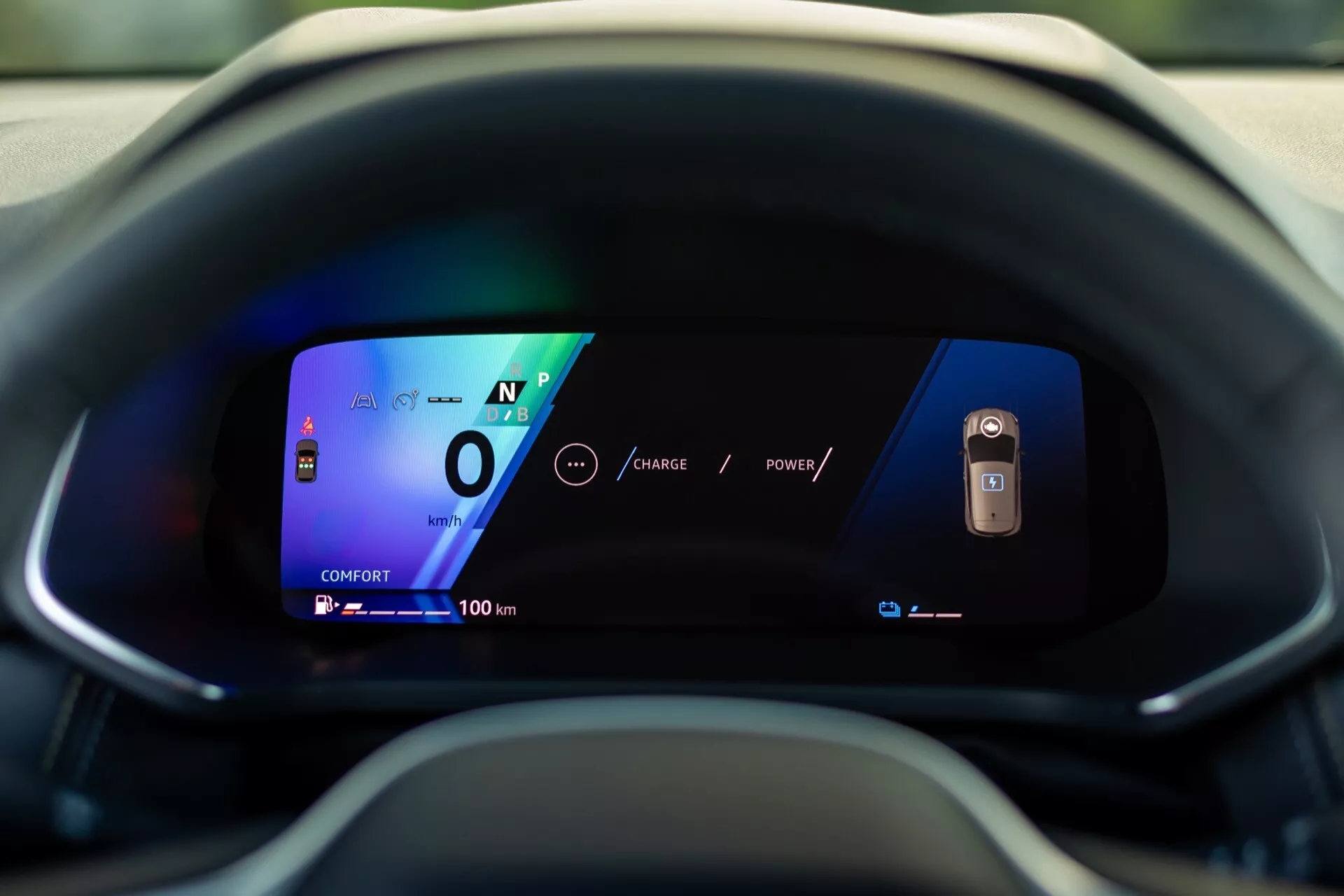 Zbliżenie cyfrowego zestawu wskaźników w Renault Symbioz 2024, widziane z perspektywy siedzenia kierowcy. Wyświetlacz z żywymi kolorami i wyraźną grafiką na zakrzywionym ekranie pokazuje samochód w neutralnym biegu z prędkością 0 i zasięgiem 100 km, podkreślając jego zaawansowaną, prawdopodobnie elektryczną technologię i nowoczesny design interfejsu użytkownika.