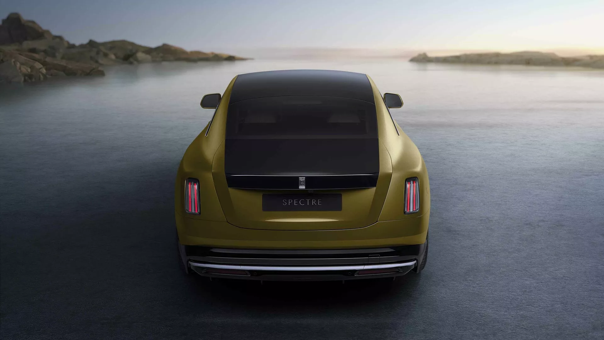 Rolls-Royce Spectre 1. generacji 2023 w metalicznym złocie uchwycony z perspektywy tylnej o złotej godzinie, podkreślający jego diody LED tylne światła, aerodynamiczny design bagażnika, polerowany tylny zderzak, podwójny system wydechowy i umiejscowiony na tle spokojnego wybrzeża.