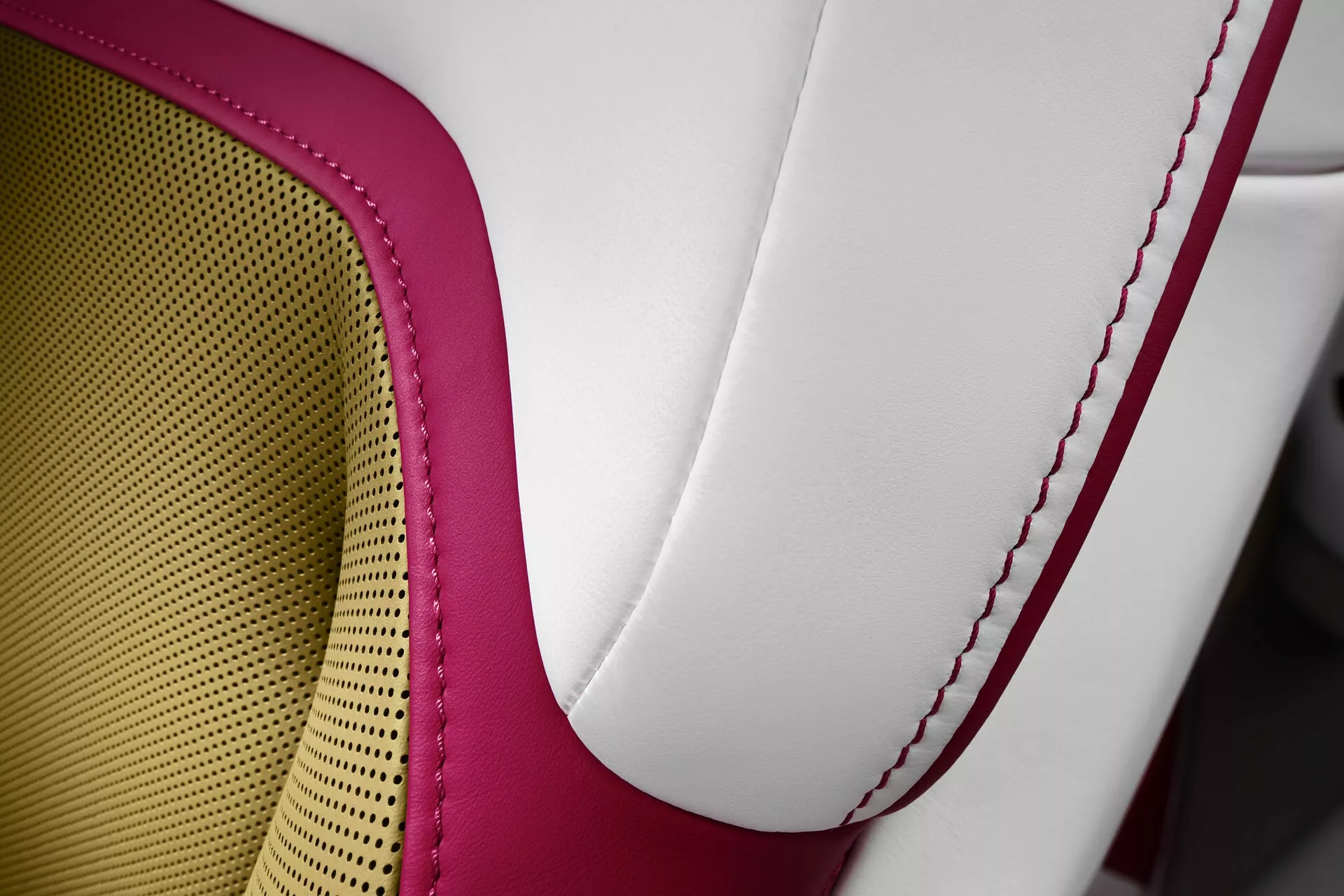 Zbliżenie na siedzenie Rolls-Royce Spectre 2023 prezentujące tapicerkę z wysokiej jakości dwukolorowej skóry, czerwone kontrastowe szwy i wzór plastra miodu dla oddychalności i komfortu, uosabiające luksus i rzemiosło.