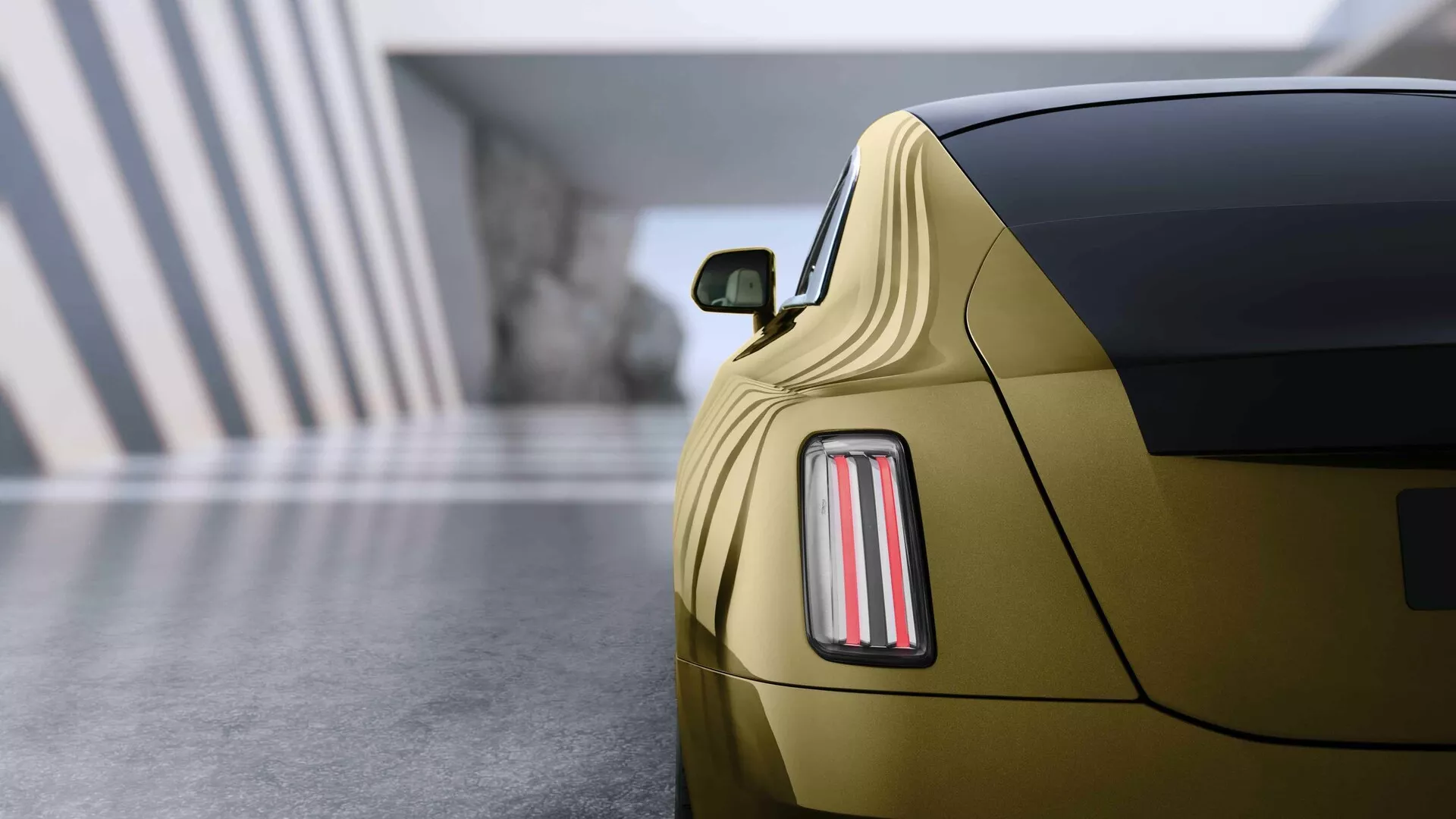Rolls-Royce Spectre 2023, 1. generacja, prezentuje zbliżony widok z tyłu na sofistykowany design świateł LED, metaliczne złote wykończenie i sportowy profil coupé w scenerii salonu