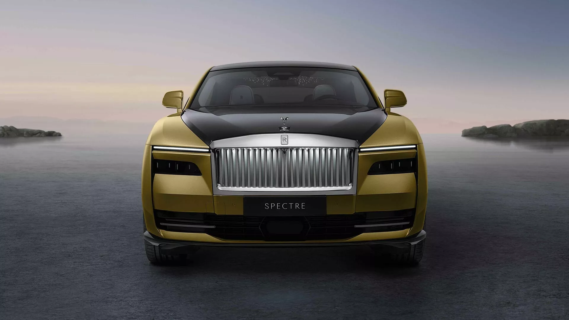 Przedni widok Rolls-Royce Spectre 2023 z wyeksponowaną atrapą chłodnicy, emblematem, reflektorami LED i metalicznym wykończeniem z zaawansowanymi funkcjami na spokojnym tle