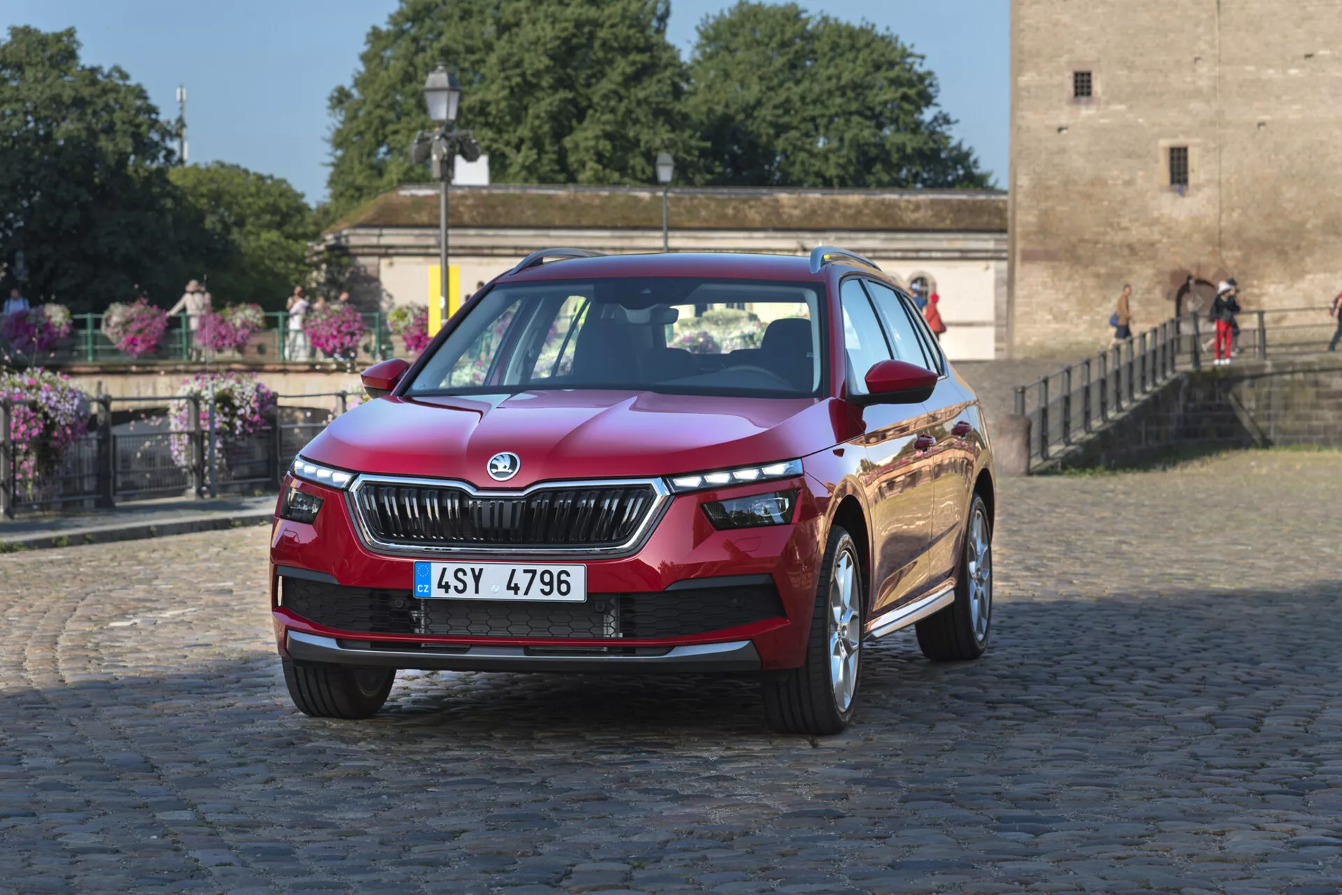 Skoda Kamiq 2019 w głębokim metalicznym czerwonym kolorze, prezentująca cechy takie jak grill, reflektory LED i felgi aluminiowe na miejskim tle z bruku