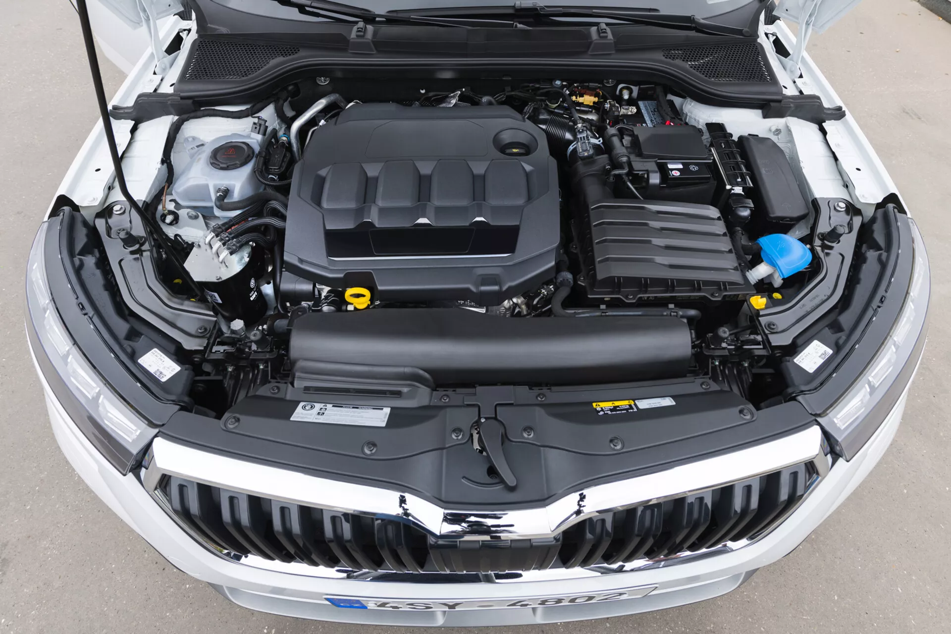 Widok z lotu ptaka na komorę silnika Skoda Kamiq 2019 z otwartą maską pokazujący pokrywę silnika, system dolotu powietrza, baterię, zbiornik płynu chłodniczego i różne inne komponenty wyraźnie widoczne, idealne do edukacji na temat technologii motoryzacyjnych i konserwacji pojazdów