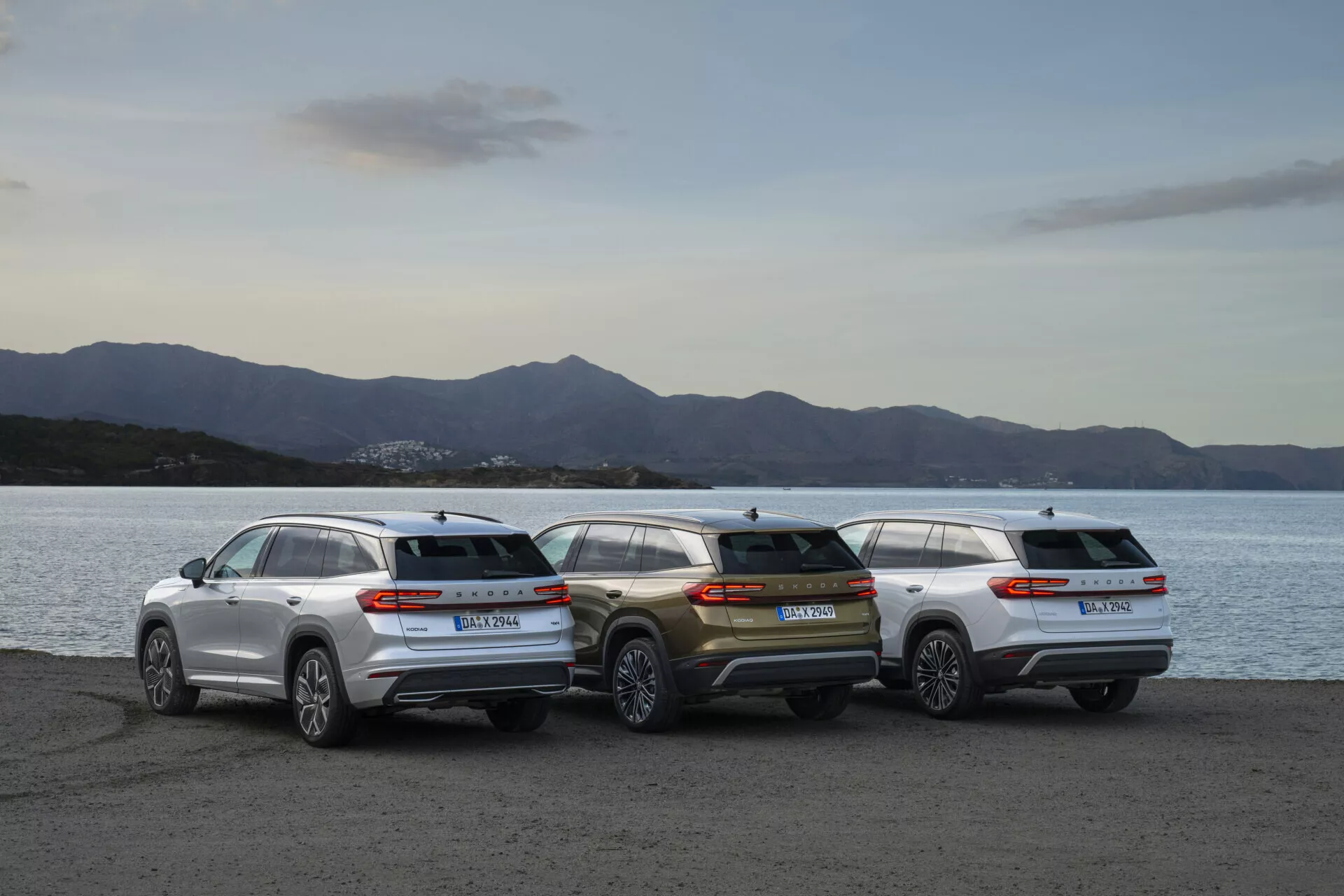 Zestawienie Skoda Kodiaq 2024 z trzema SUV-ami zaparkowanymi na nabrzeżu o zmierzchu, ukazujące tylne profile i estetykę projektowa przeciwko tle łagodnie oświetlonego krajobrazu