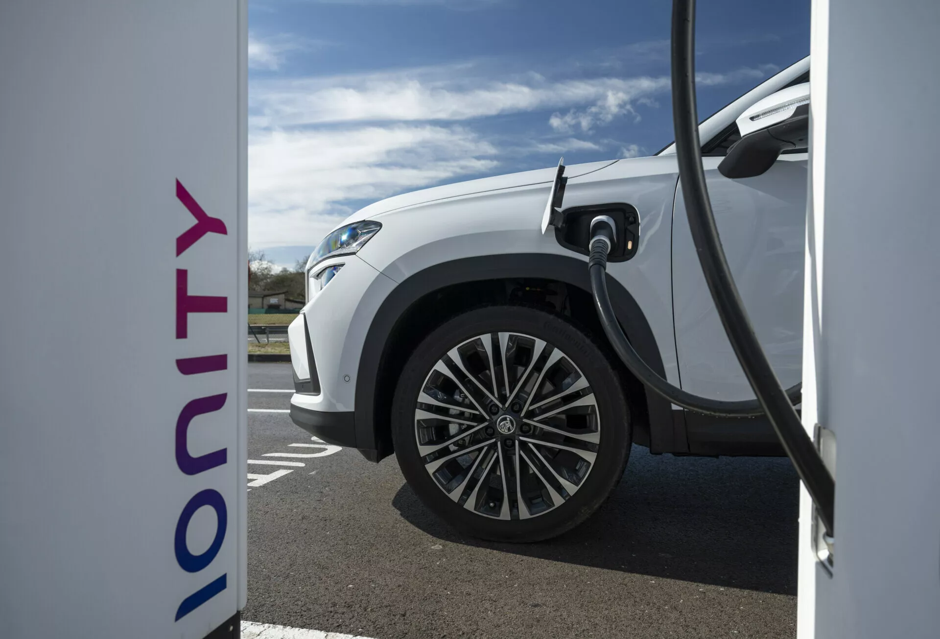 Zbliżenie na bok białego elektrycznego pojazdu Skoda Kodiaq 2024 podczas ładowania na stacji Ionity, pokazujące technologię szybkiego ładowania i nowoczesny design