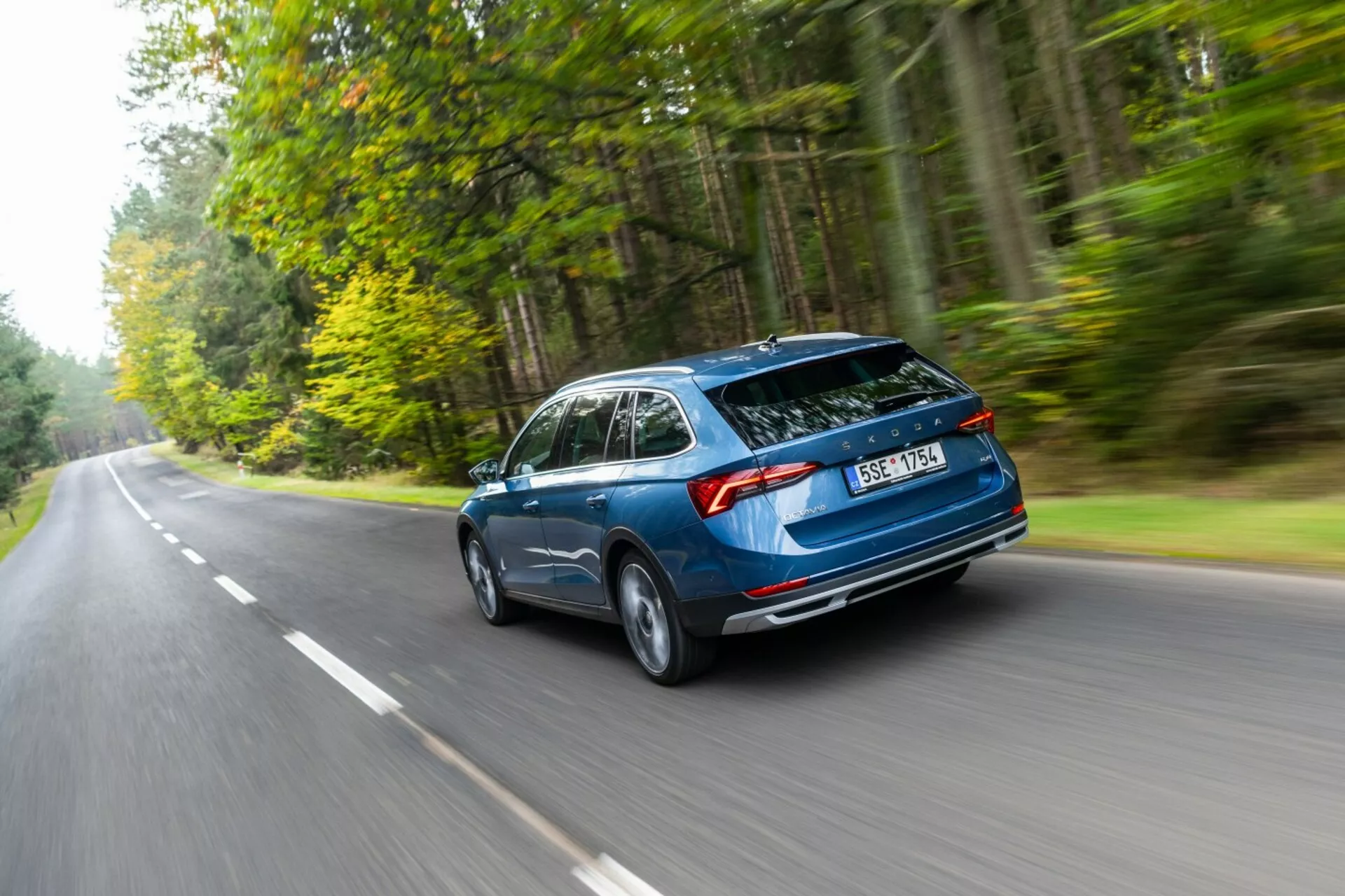 Skoda Octavia kombi 2017 w ruchu, uchwycona z tylnego trzykwartalnego kąta podkreślającego aerodynamiczny projekt, tylny bagażnik typu hatchback i poziome tylne światła na drodze otoczonej lasem