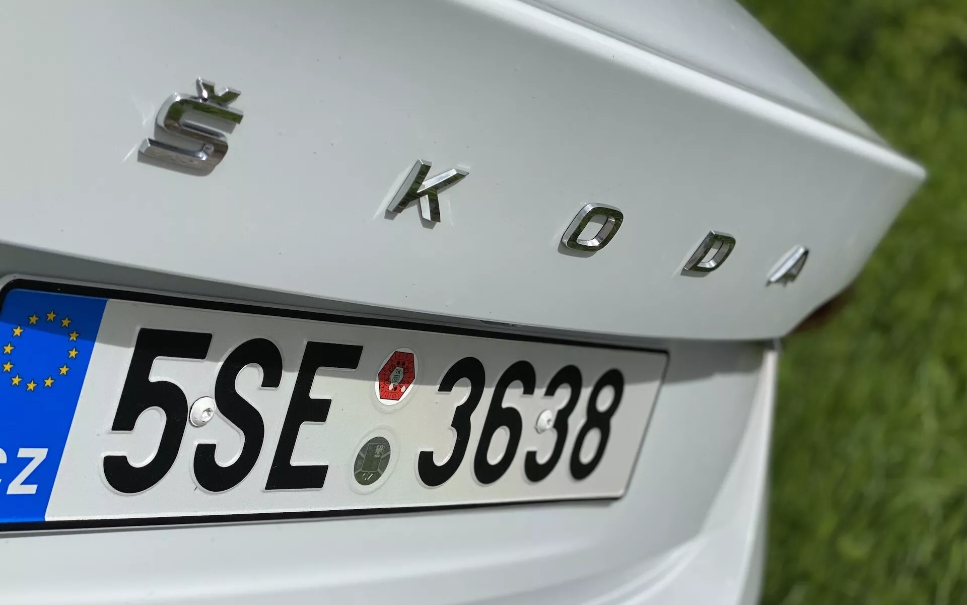 Zbliżenie na tylną część limuzyny Škoda Octavia 2020, koncentrujące się na klapie bagażnika, tylnej tablicy rejestracyjnej z europejskim identyfikatorem 'CZ' oraz chromowanymi literami 'SKODA'. Funkcje obejmują cztery okrągłe czujniki parkingowe nad tablicą rejestracyjną, wspomagające manewrowanie pojazdem.
