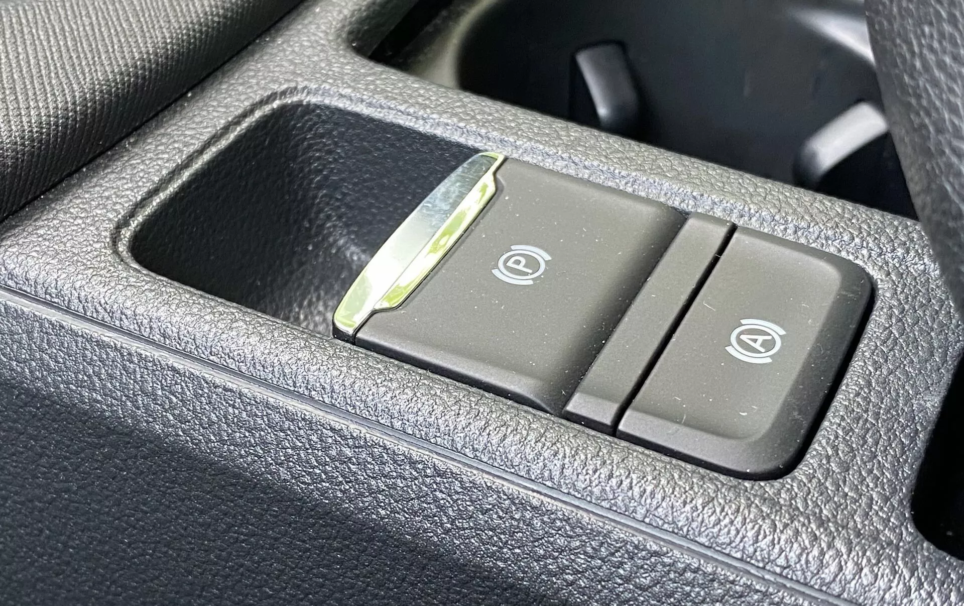 Zbliżenie panelu sterowania wewnątrz pojazdu Skoda Octavia 2020, pokazujące przyciski podgrzewanych i wentylowanych siedzeń na ciemnym, ziarnistym materiale przypominającym skórę. Lewy przycisk ma ikonę podgrzewanego siedzenia, a prawy przycisk pokazuje ikonę wentylowanego siedzenia, z małą lampką kontrolną LED między przyciskami.