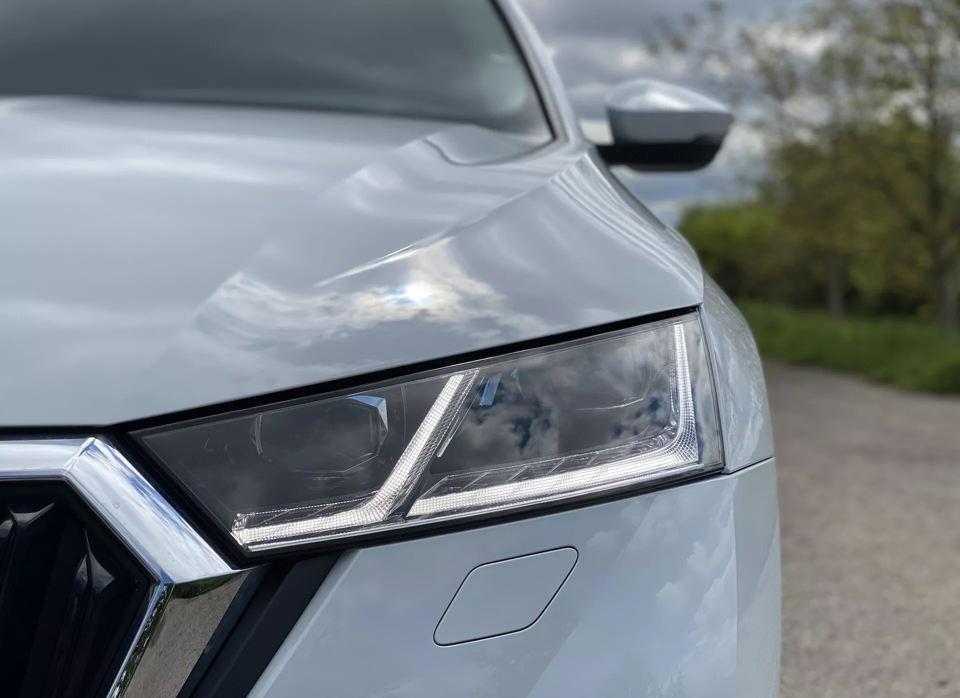 Zbliżenie na Skoda Octavia Limousine 2020, koncentrujące się na złożonym lewym przednim reflektorze z elementami LED i światłami do jazdy dziennej. Widoczna jest część chromowanej osłony chłodnicy i maski samochodu o aerodynamicznych krzywiznach, co tworzy nowoczesny, stylowy wygląd wskazujący na zaawansowaną technologię i design premium.