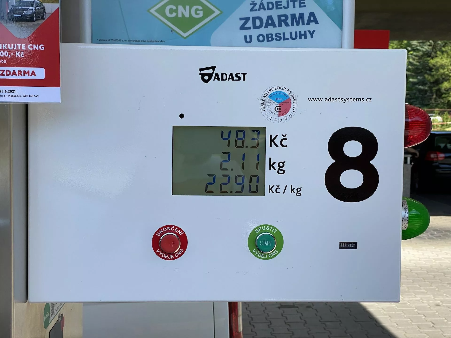 Wyświetlacz dystrybutora sprężonego gazu ziemnego (CNG) na stacji benzynowej pokazujący 40,1 Kč za ilość paliwa, 2,01 kg jako wagę gazu i cenę za kilogram wynoszącą 22,90 Kč. Wyświetlacz zawiera loga marek i identyfikator numeryczny 8, z otoczeniem zewnętrznym sugerowanym przez znak myjni samochodowej lub usługi w tle.