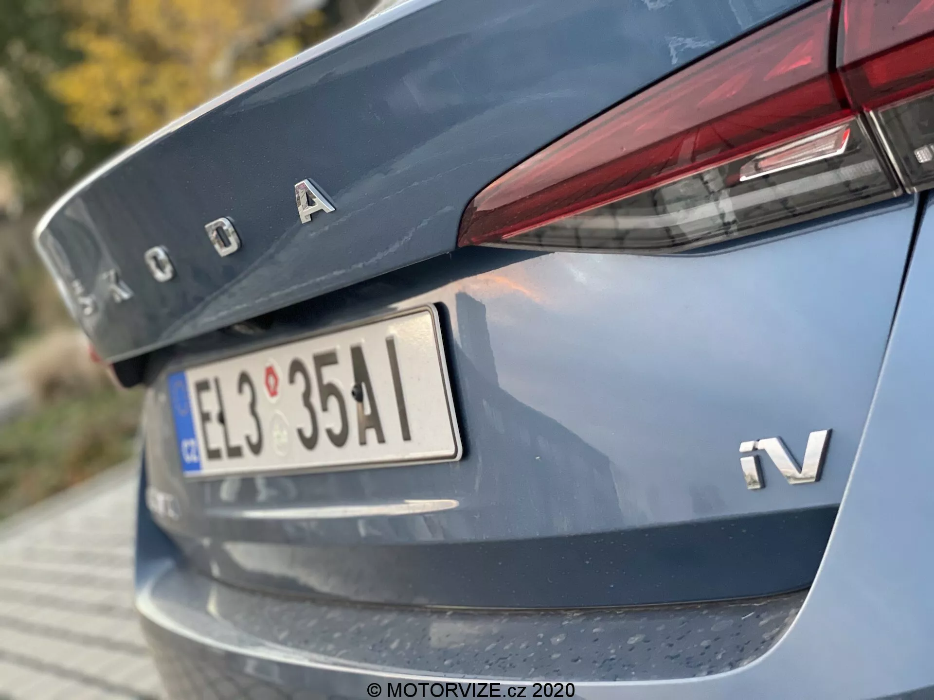 Zbliżenie tylnej części Škoda Octavia Limousine 2020, uchwyconej z niskiego kąta, skupiającą się na klapie bagażnika, części tylnego zderzaka, z chromowanym logo Škoda, odznaką iV dla wariantu hybrydowego lub elektrycznego, tablicą rejestracyjną w stylu europejskim, wąskimi horyzontalnie zorientowanymi tylnymi światłami rozciągającymi się na klapie bagażnika i odblaskowym paskiem na tylnym zderzaku.