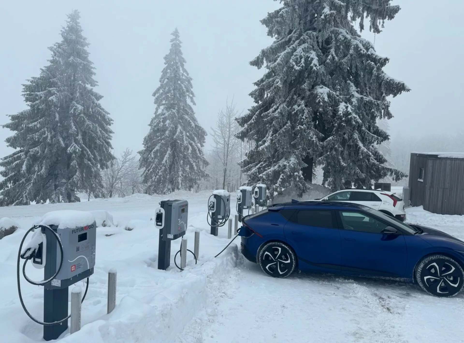 Niebieska limuzyna Skoda Octavia 2020 ładowana na stacji pojazdów elektrycznych, widok skośny od tyłu, podkreślająca jej felgi aluminiowe, port ładowania i design gotowy na zimę w śnieżnych warunkach.