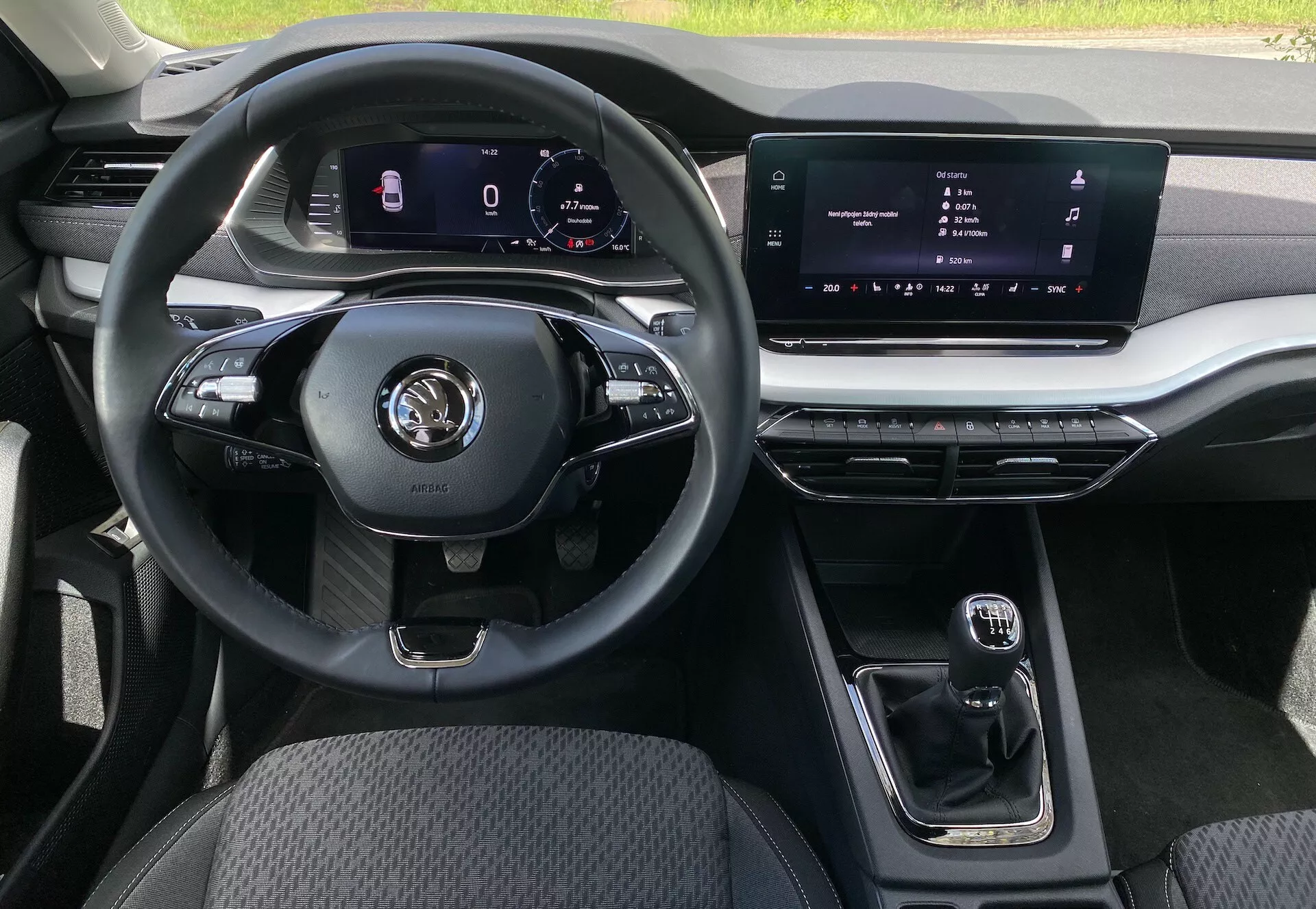Wnętrze sedana Škoda Octavia 2020 z perspektywy siedzenia pasażera, podkreślone wielofunkcyjną kierownicą trzyramienną z różnymi przyciskami do sterowania multimediami i połączeniami w trybie głośnomówiącym, cyfrowym zestawem wskaźników do nawigacji i statystyk auta, centralnym dotykowym ekranem informacyjno-rozrywkowym, kompaktową automatyczną skrzynią biegów, metalowymi akcentami na kratkach wentylacyjnych i systemie informacyjno-rozrywkowym, trwałą tapicerką z tkaniny na siedzeniu kierowcy i dostosowywanym oświetleniem ambientowym.