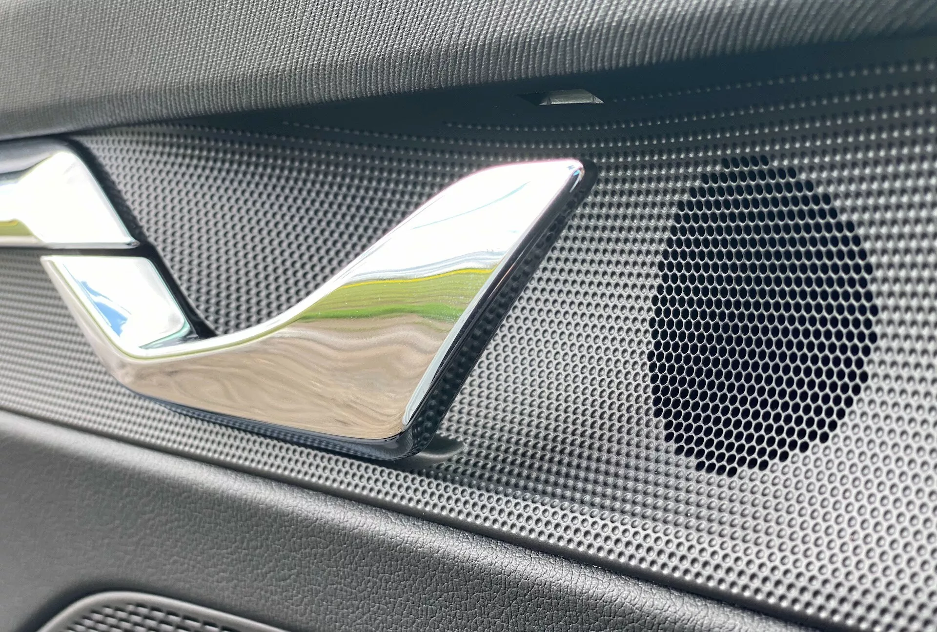 Zbliżenie wnętrza Skoda Octavia limuzyna 2020, z wyróżniającą się chromowaną klamką drzwi i kratką głośnika o wzorze plastra miodu, wykonaną z teksturowanego, możliwie z włókna węglowego materiału, podkreślając luksus i wysokiej jakości system audio.