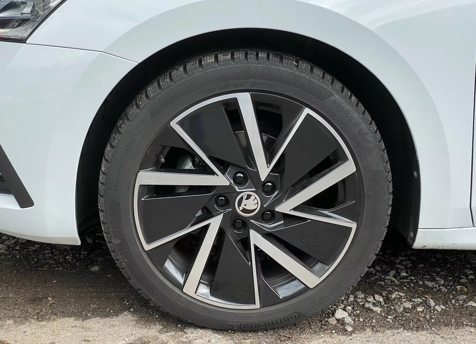 Zbliżenie przedniego koła limuzyny Skoda Octavia 2020, prezentujące nowoczesne pięcioramienne felgi aluminiowe z dwukolorowym wykończeniem i mechanicznie wykonanymi ramionami, uchwycone pod kątem 45 stopni, podkreślając dynamiczny, turbinowy design i widoczny bieżnik opony całorocznej.