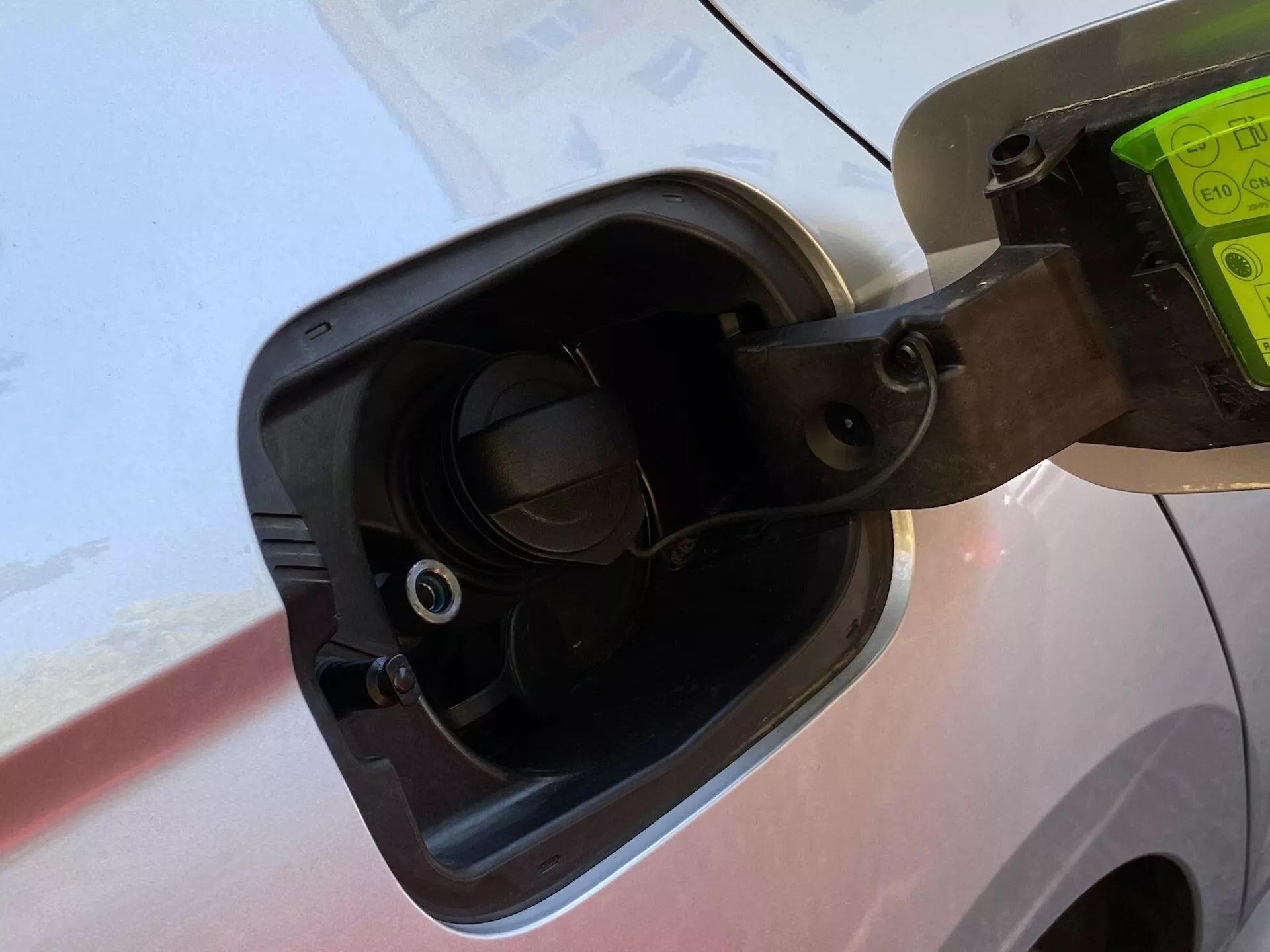 Zbliżenie na obszar wlewu paliwa w samochodzie Skoda Octavia Limousine 2020, przedstawiające otwartą nakrętkę paliwa przymocowaną elastycznym paskiem, otaczające szczegóły nadwozia pojazdu i wbudowaną szyjkę wlewu paliwa z widocznym zaworem, wszystko widziane pod lekkim kątem w dół.