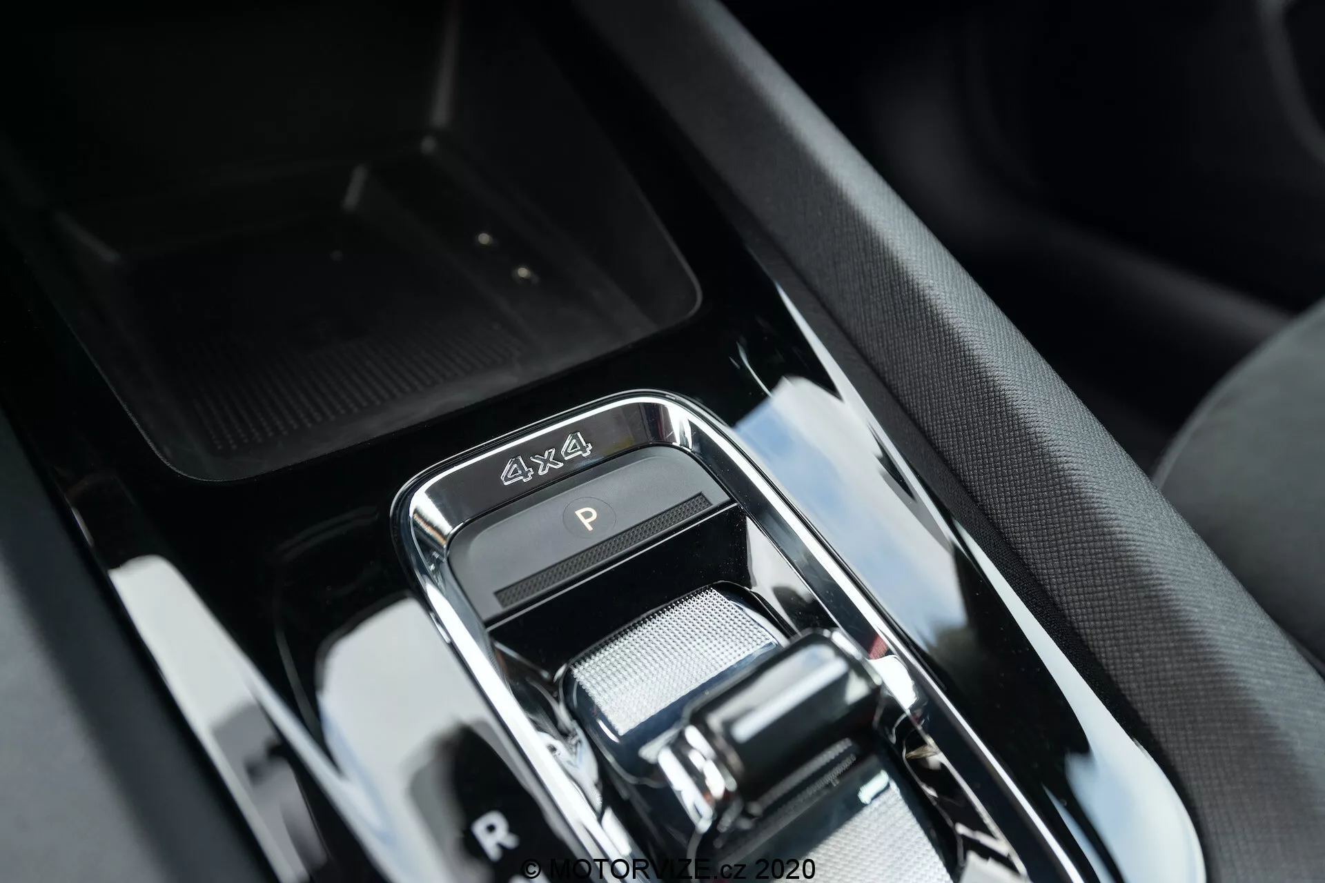 Zbliżenie na obszar dźwigni zmiany biegów w luksusowym wnętrzu Skoda Octavia Scout 2020, z nowoczesnym elektronicznym selektorem biegów z chromowanym wykończeniem, emblematem 4x4, eleganckim wykończeniem w połyskującym czarnym kolorze i wyrafinowanym designem konsoli środkowej z okolicznymi przyciskami i zasugerowanym schowkiem.