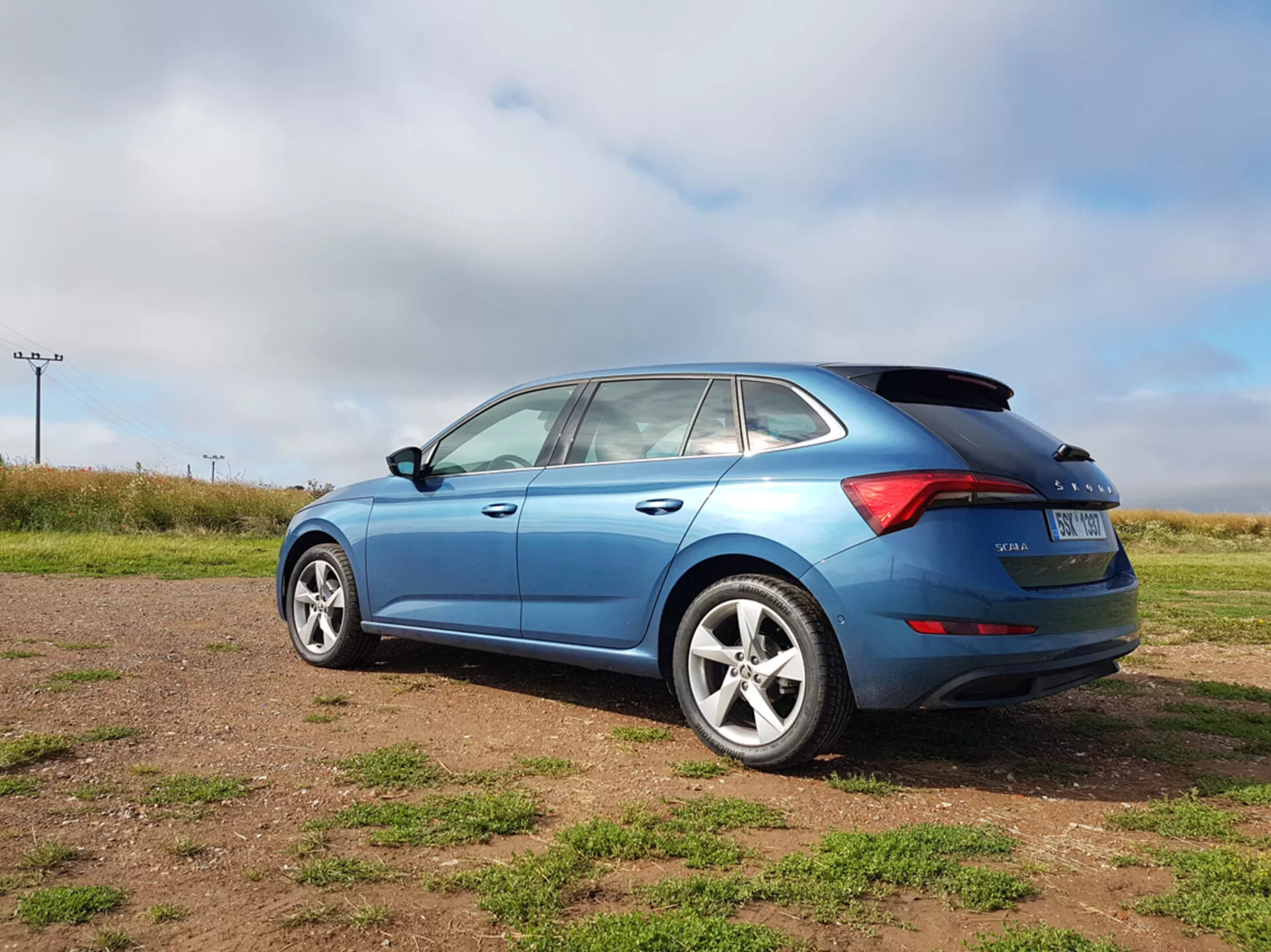 Niebieskie hatchback Skoda Scala 2019 pokazujące elementy projektu boczne i tylne, w tym kształt okien, tylne światła LED i koła ze stopów, sfotografowane z trzykwartalnego tylnego kąta na trawiastym terenie