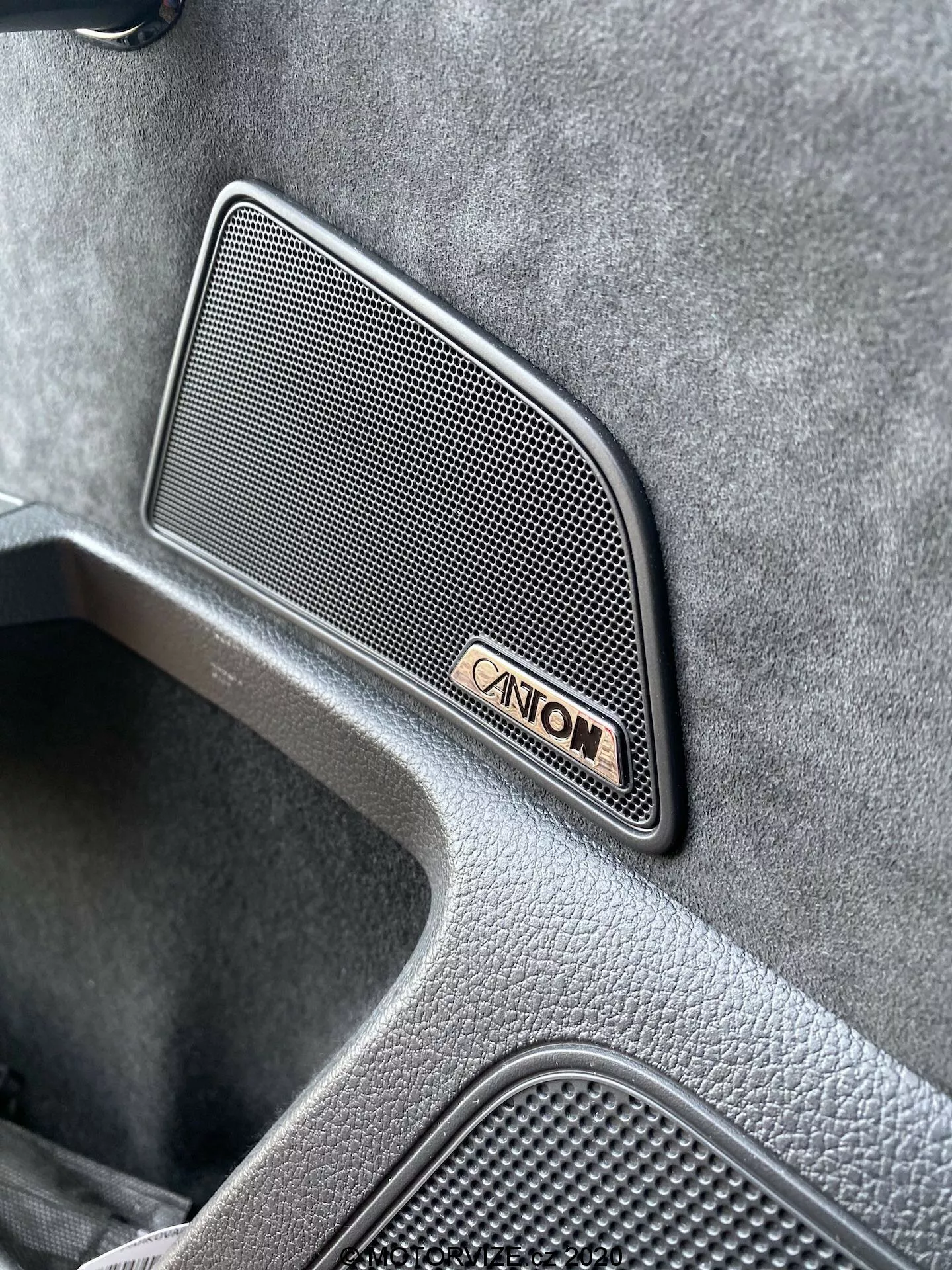 Zbliżenie widoku pod kątem wnętrza Skody Superb Limousine 2019, podkreślającego wysokiej jakości kratkę głośnika Canton o siatkowym wzorze trapezoidalnym, umieszczoną na panelu drzwi, w towarzystwie znaku Canton, pokazującą wysokiej klasy teksturowane wykończenie i zagłębiony obszar wskazujący na luksusowy design pojazdu.