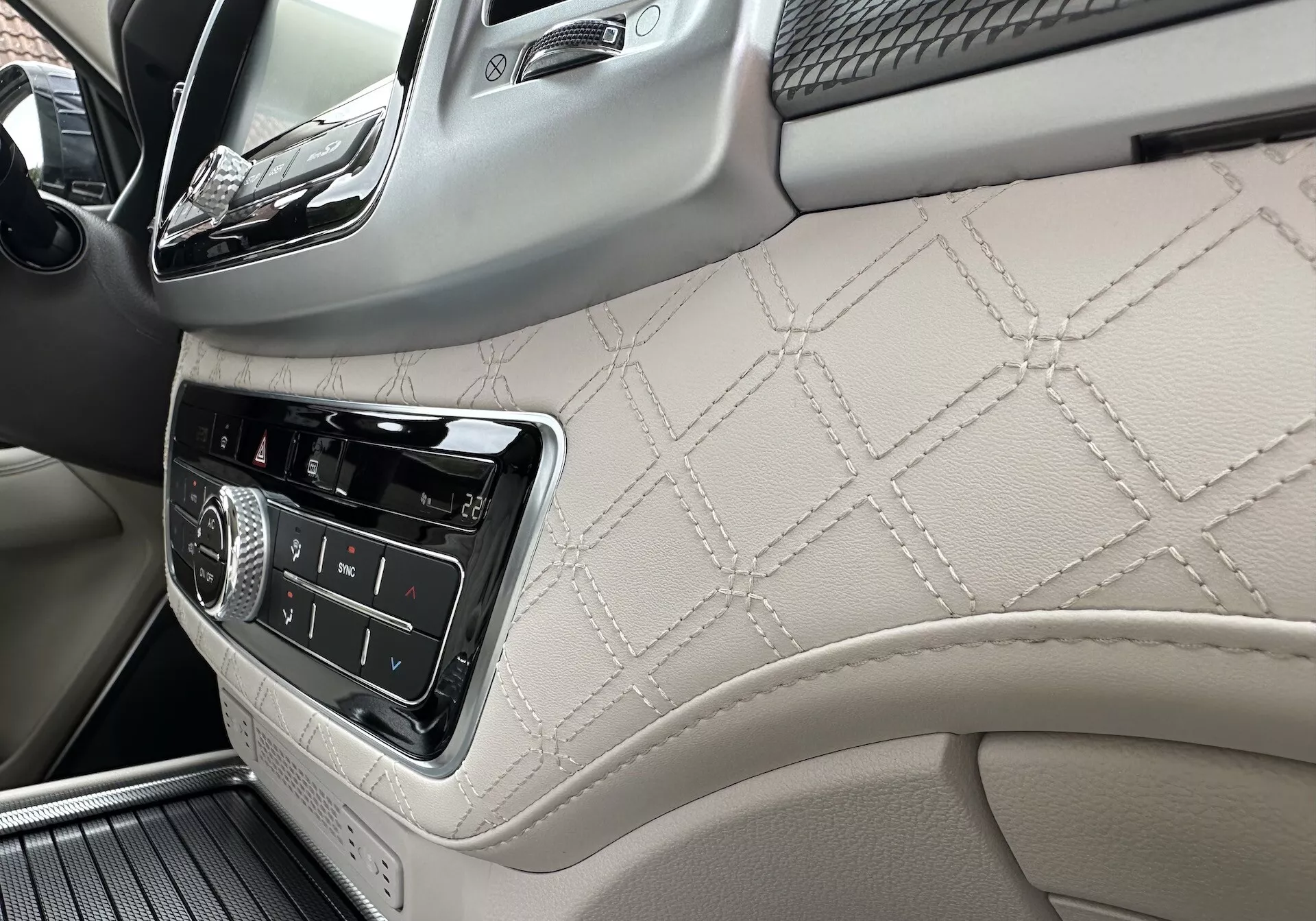 Wnętrze SsangYong Rexton 2021 skupiające się na desce rozdzielczej po stronie pasażera i części przedniego panelu drzwiowego z skórą z pikowaniami w kształcie diamentu, kontrolami systemu infotainment i luksusowymi detalami z drewna