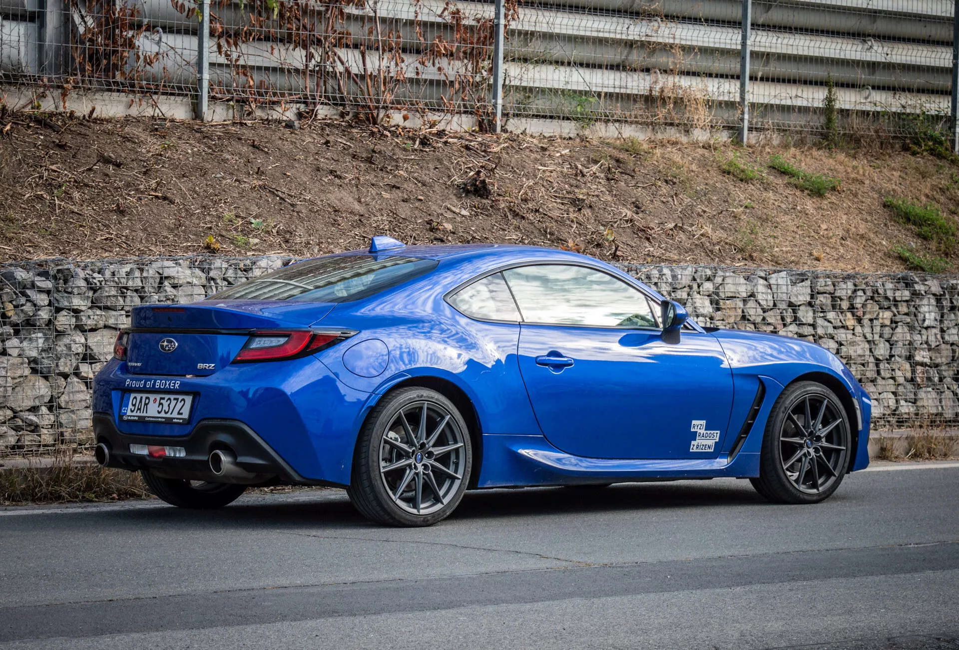 Sportowe coupé Subaru BRZ 2023 w jasnoniebieskim kolorze z aerodynamicznym designem zaparkowane na ulicy, z akcentem na luk koła tylnego, tylne światła, krzywiznę tylnej szyby do pokrywy bagażnika, rzeźbione linie, pochylony dach, wieloramienne felgi aluminiowe, hamulce wysokiej wydajności, niskoprofilowy tylny spoiler, podwójne rury wydechowe w tylnym dyfuzorze, lusterka boczne w kolorze nadwozia i sportową, długą maskę.