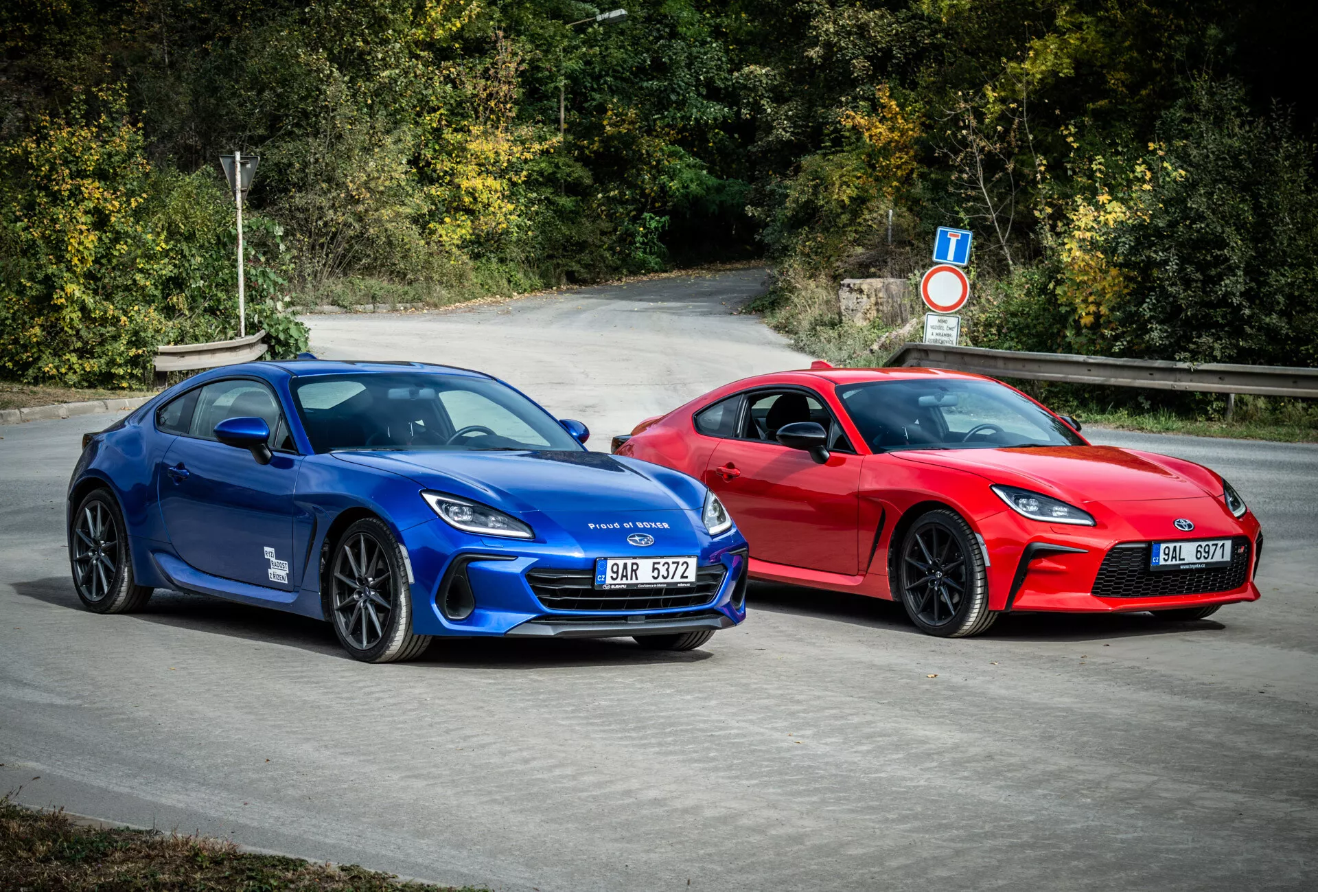 Sportowe coupé Subaru BRZ 2023 w kolorach niebieskim i czerwonym z aerodynamicznym designem i funkcjami zwiększającymi wydajność, zaparkowane na zewnątrz w otoczeniu naturalnej zieleni