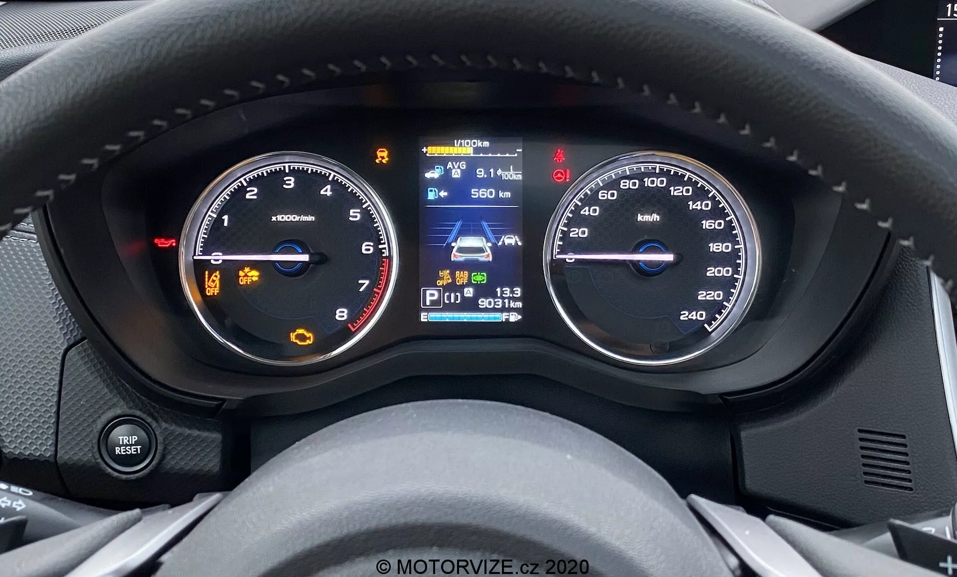 Zbliżony widok wnętrza Subaru Forester 2020 z perspektywy kierowcy, ukazujący analogowy obrotomierz z nieruchomą wskazówką powyżej 0 obr./min., wyświetlacz cyfrowy z mapą nawigacyjną, pełny wskaźnik paliwa i funkcje wspomagania kierowcy, wraz z analogowym prędkościomierzem skalibrowanym do 260 km/h, wskazując, że pojazd jest w stanie spoczynku. Nowoczesny design z zintegrowanymi wyświetlaczami cyfrowymi.
