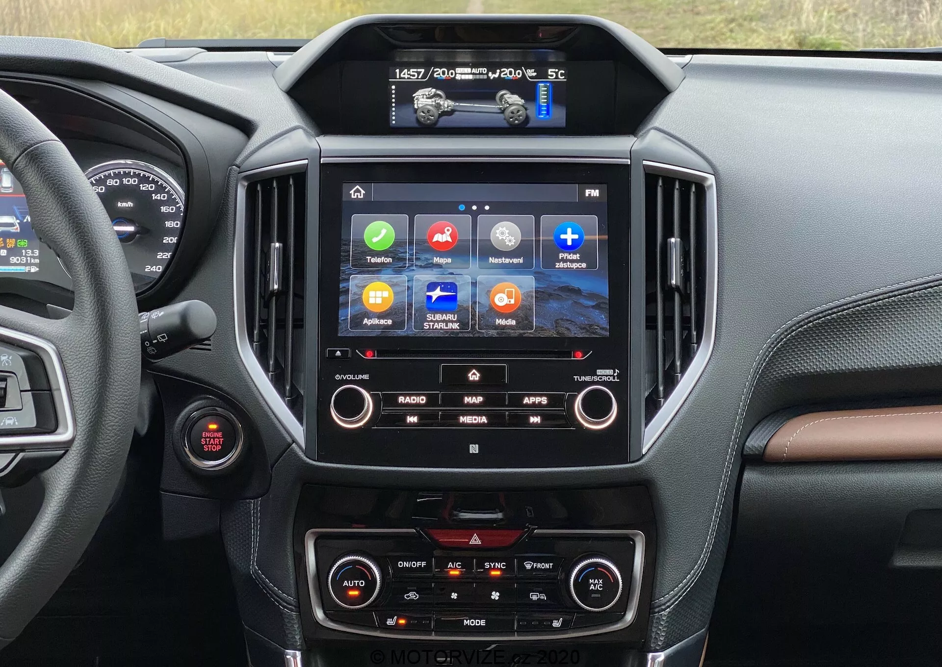 Widok wnętrza Subaru Forester 2020 skupiający się na konsoli centralnej i systemie infotainment. Ekran dotykowy pokazuje kolorowe ikony dla Radia, Mapy, Aplikacji i Mediów, wskazując funkcje takie jak nawigacja GPS, integracja aplikacji i odtwarzanie multimediów. Poniżej widoczne są pokrętła klimatyzacji dwustrefowej. Przez okno widać fragment obszaru kierowcy z czerwonym przyciskiem, prawdopodobnie do uruchamiania/zatrzymywania silnika. Projekt wnętrza wykorzystuje ciemne i brązowe materiały podobne do skóry z przeszyciami, nadając wnętrzu luksusowy charakter.