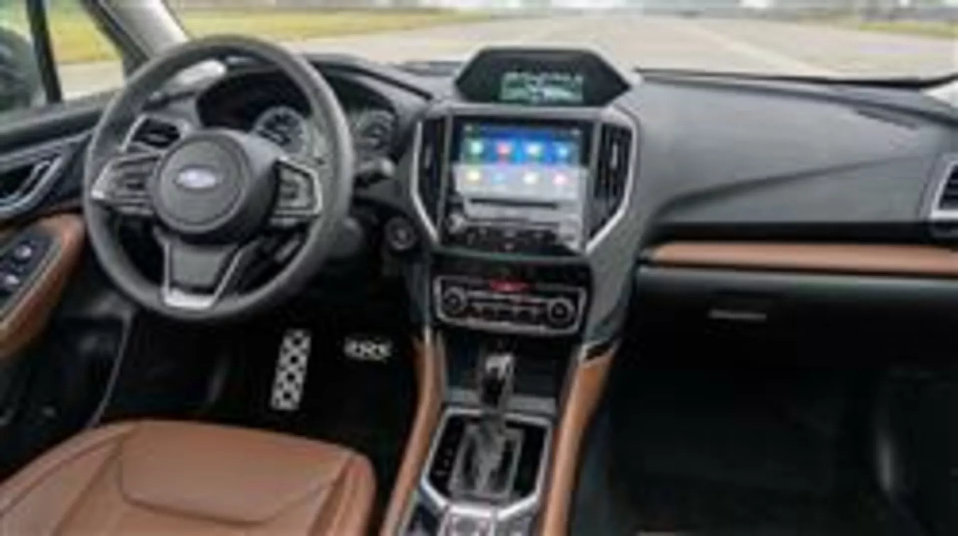 Wnętrze Subaru Forester 2015 z deską rozdzielczą, wielofunkcyjną kierownicą, systemem infotainment z ekranem dotykowym, selektorem automatycznej skrzyni biegów i akcentami z materiałów luksusowych widziane z boku pasażera