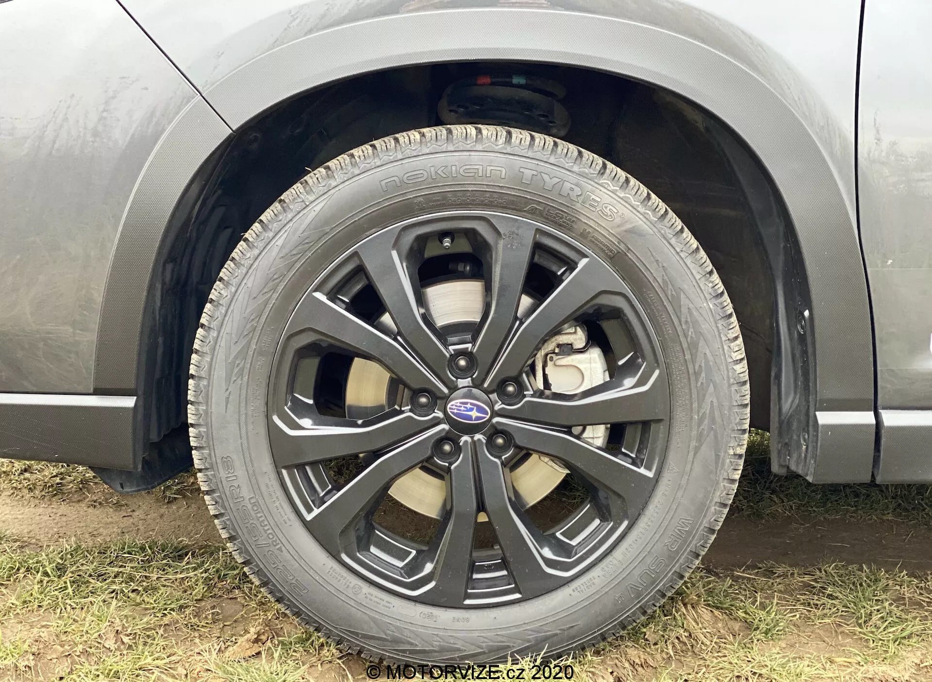 Zbliżenie na przednie koło pasażera Subaru Forester 2020, ukazujące wieloramienną felgę z dwukolorowym wykończeniem, widoczną oponą Goodyear Eagle, deklem centralnym z logo Subaru, zaciskiem hamulcowym sugerującym system hamulców tarczowych i widocznymi elementami zawieszenia, podkreślające szczegółowy design koła i charakterystyki wydajnościowe pojazdu.