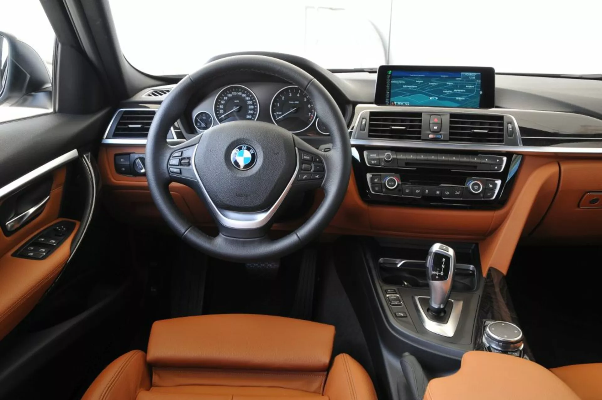 Przedni widok wnętrza BMW Outback 2003 pokazujący obszar kierowcy i konsolę środkową z zamontowanymi elementami sterującymi na kierownicy, analogowe tarcze i centralny wyświetlacz cyfrowy na desce rozdzielczej, szerokoekranowy system infotainment i fotele tapicerowane skórą
