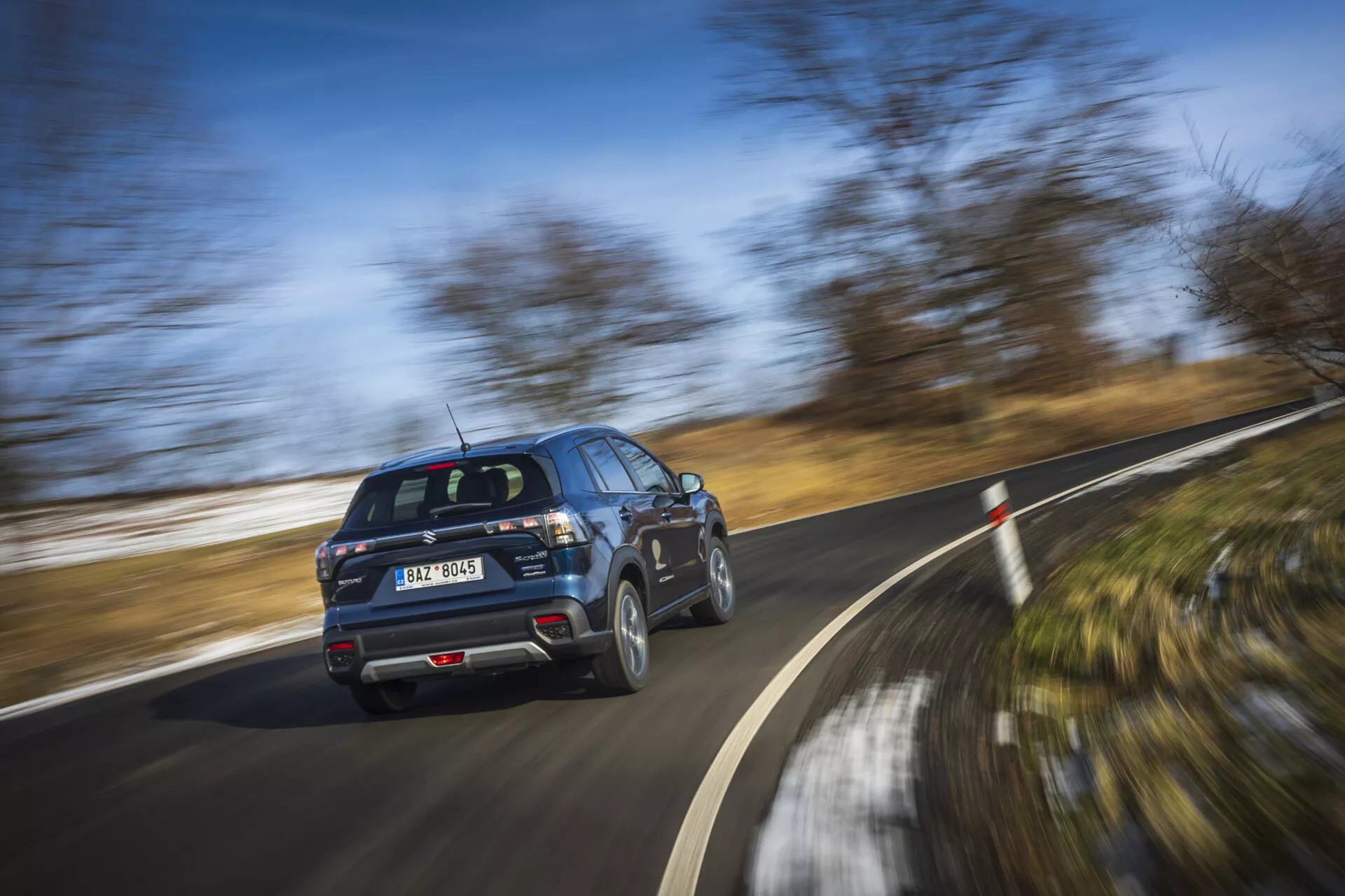 Nowoczesny SUV Suzuki S-Cross 2022 w ruchu, pokazujący profil z tyłu trzy czwarte z obracającymi się kołami w jasny dzień
