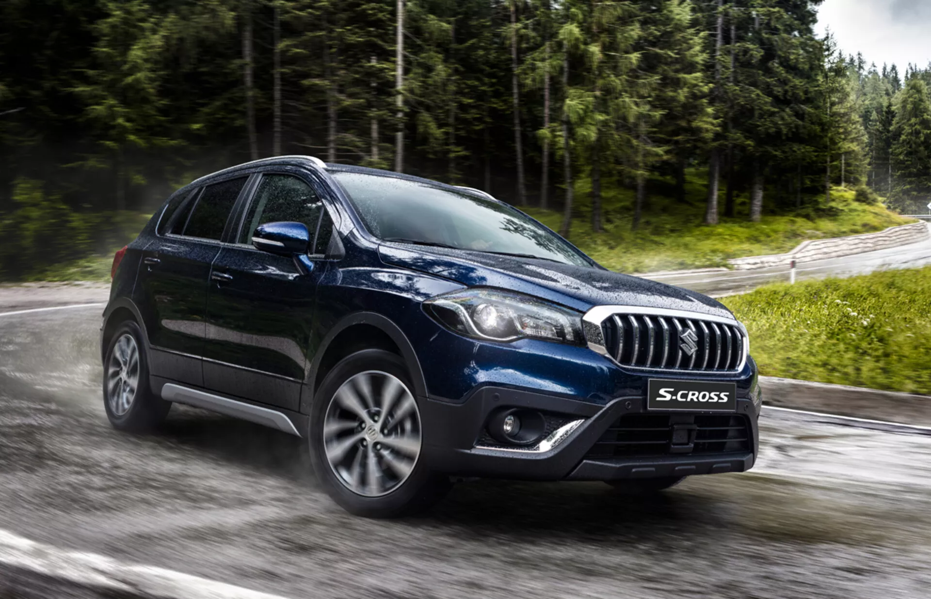 Suzuki S-Cross 2022 ujęty z przedniego kąta trzy czwarte, podkreślający jego chromowaną atrapę, nowoczesne reflektory LED lub HID, wieloramienne felgi ze stopu i robustną sylwetkę crossovera na mokrej drodze otoczonej zielenią, sugerujący zaawansowaną technologię i zdolności do jazdy we wszelkich warunkach pogodowych.