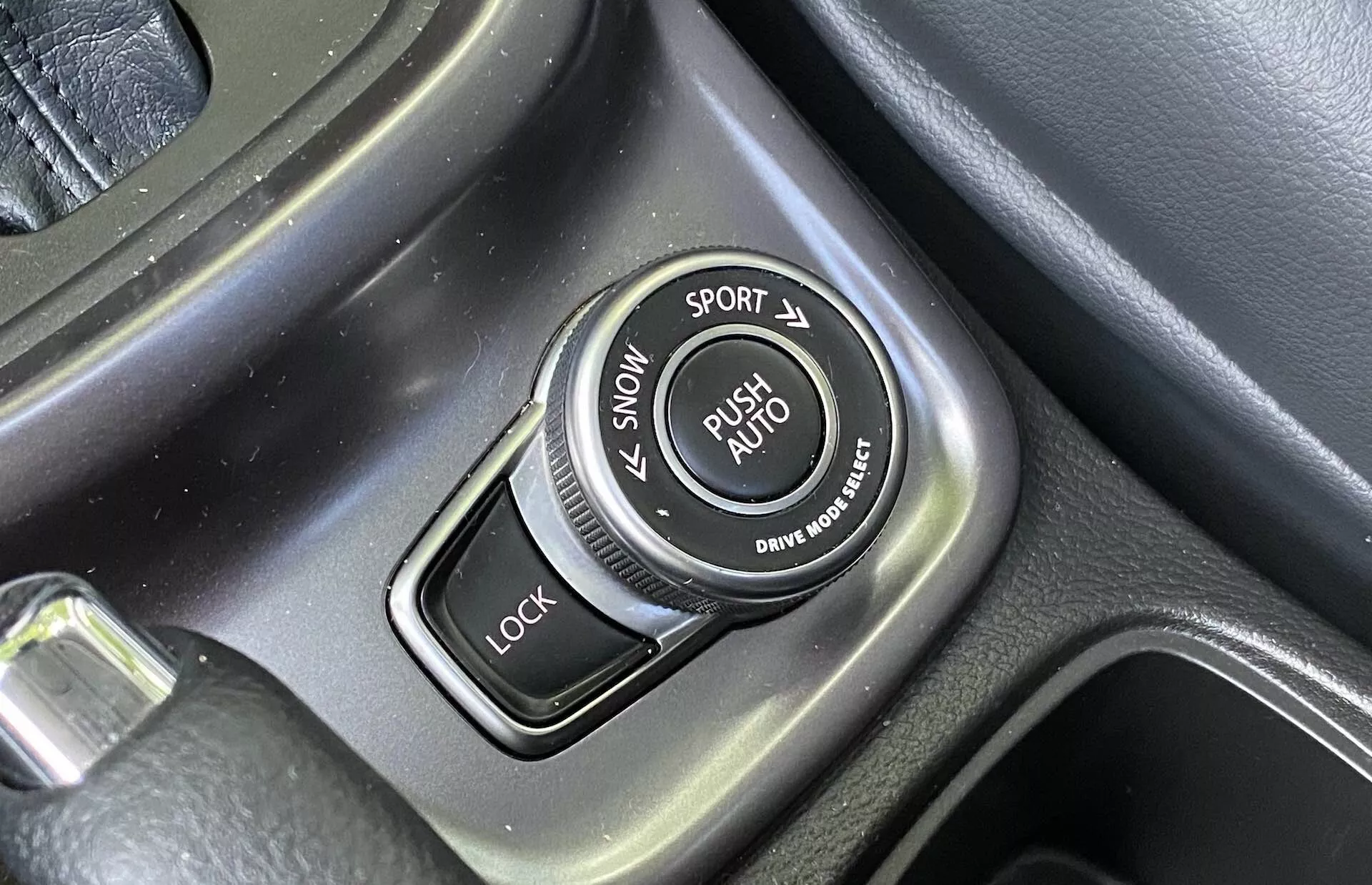 Zbliżenie pokrętła wyboru trybu jazdy w konsoli centralnej Suzuki Vitara 2018 z etykietami trybów ŚNIEG, SPORT, LOCK i AUTO, teksturowaną obwódką oraz szczotkowanymi metalowymi akcentami.