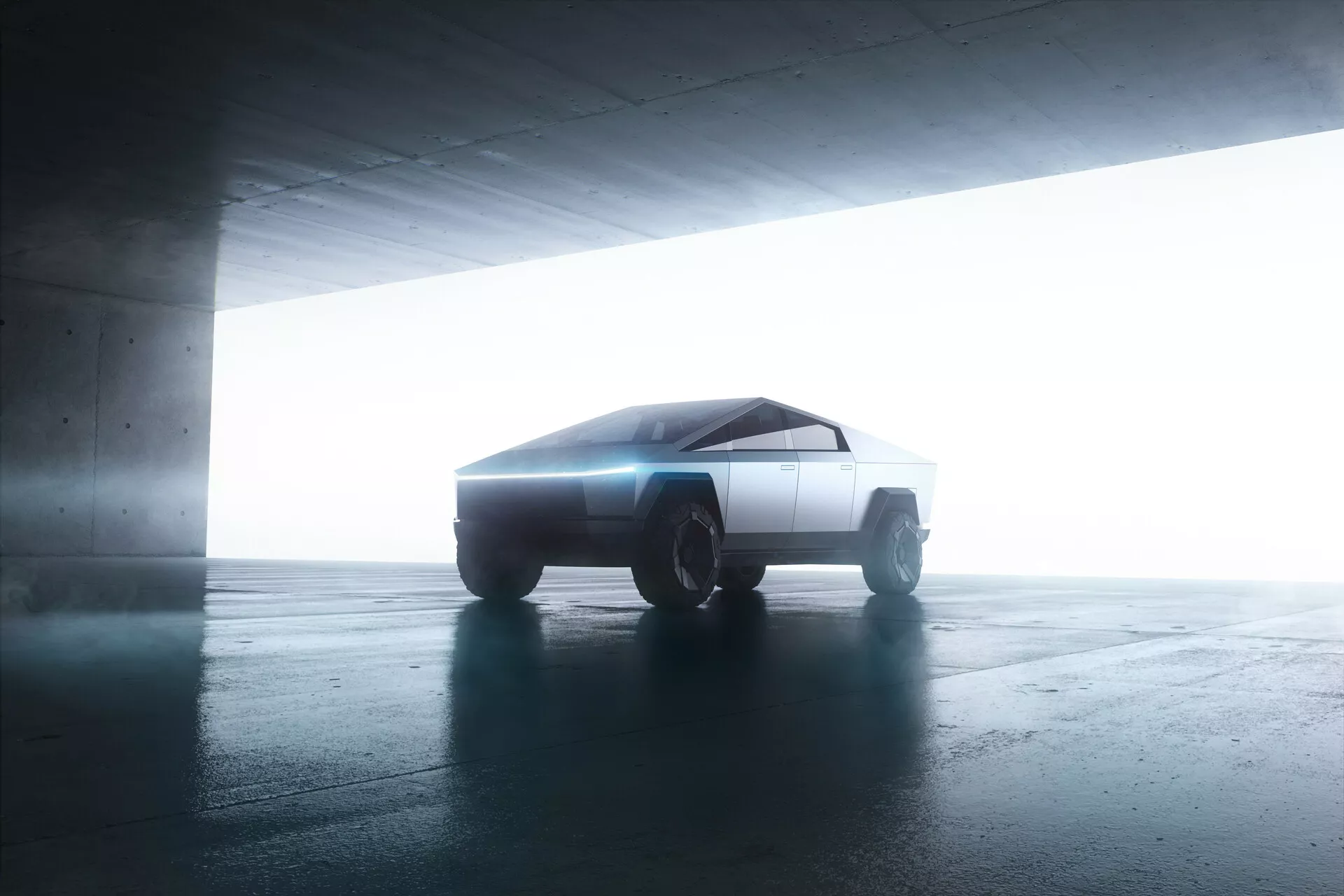 Widok boczny Tesla Cybertruck 2021 w garażu. Pojazd o futurystycznym, kanciastym designie jest lekko nachylony w stronę kamery, ukazując swoje minimalistyczne, geometryczne linie. Podświetlenie od tyłu podkreśla jego sylwetkę, tworząc efekt halo. Płaskie i ostre powierzchnie samochodu oraz solidne koła terenowe sugerują zaawansowaną, prawdopodobnie elektryczną technologię napędową.