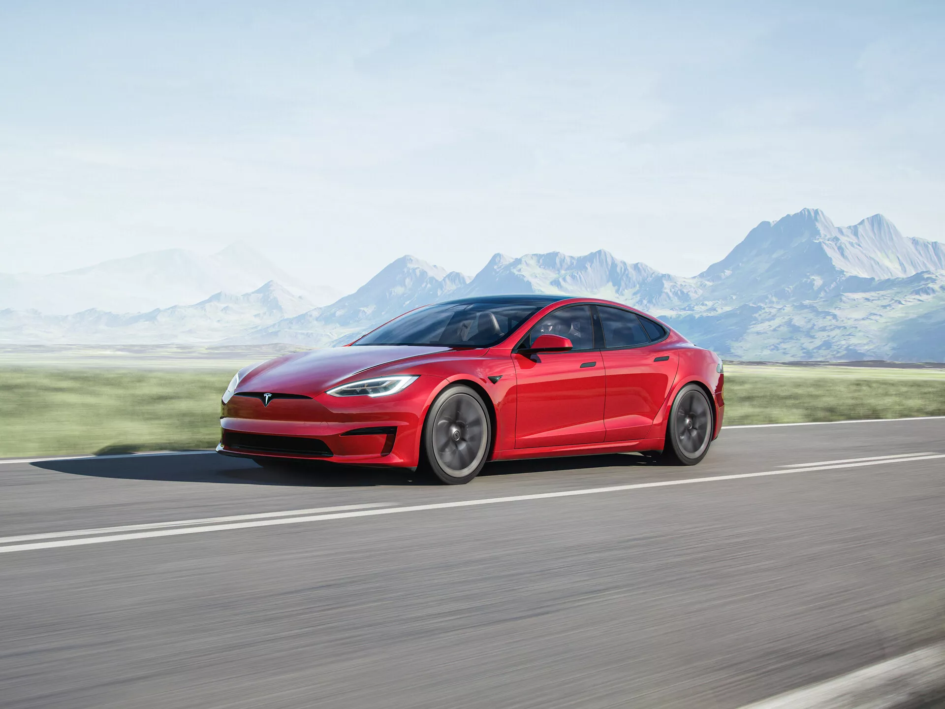 Z profilu bocznego, Tesla Model S z 2016 roku (1. generacja facelift), elektryczny sedan w kolorze czerwonym, uchwycony w ruchu. Zaprezentowano elegancki i aerodynamiczny wygląd samochodu, z gładkimi liniami od przedniego błotnika po tylną część i polerowanymi felgami. Fotografowany na asfaltowej drodze z rozmytym tłem gór i czystego nieba, co podkreśla prędkość i ruch pojazdu.