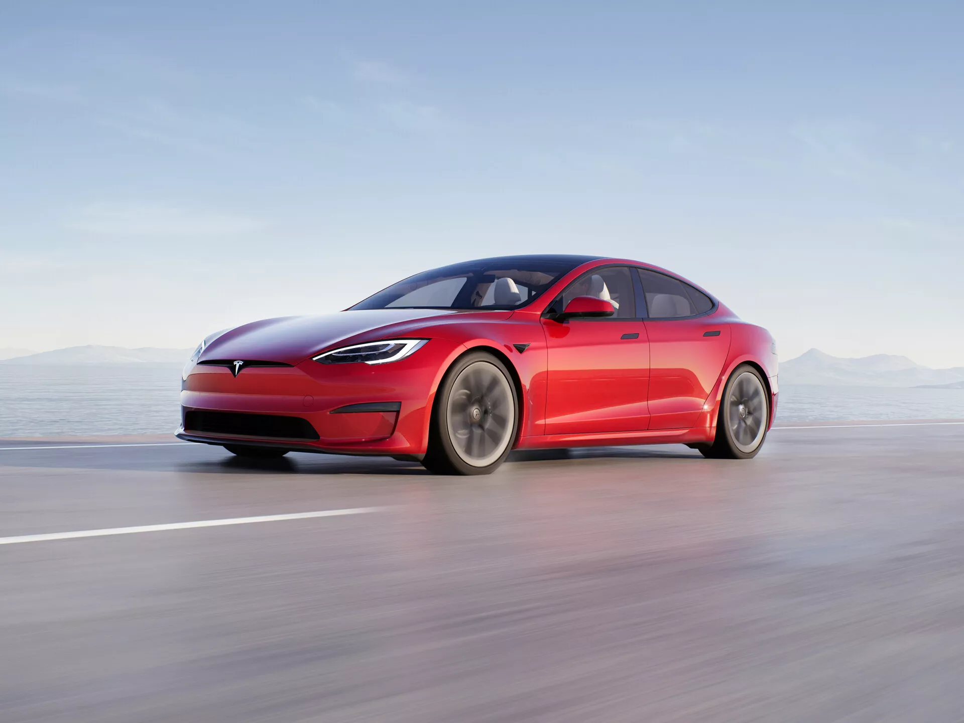Obraz przedstawia nowoczesny czterodrzwiowy sedan Tesla Model S 2016 (pierwszej generacji po liftingu) w ruchu na gładkiej drodze lub torze. Prezentowany z niskiego kąta widoku bocznego, wyraźnie widoczne są eleganckie i aerodynamiczne linie pojazdu, w tym charakterystyczny zamknięty grill, wąskie reflektory LED i gładki przedni zderzak. Design fastback z łagodnie opadającą linią dachu, wbudowanymi wysuwanymi klamkami drzwi i minimalistycznymi aerodynamicznymi lusterkami bocznymi podkreśla skupienie pojazdu na aerodynamice. Duże wieloszprychowe koła sugerują optymalizację przepływu powietrza i zmniejszenie oporu. Kompozycja używa rozmycia ruchu do ukazania wysokiej prędkości, sam samochód jest ostro ukazany na rozmytym tle. Ta profesjonalna fotografia podkreśla elektryczną naturę samochodu, zaawansowane oświetlenie, aerodynamiczny design i potencjalne funkcje wspomagania kierowcy.