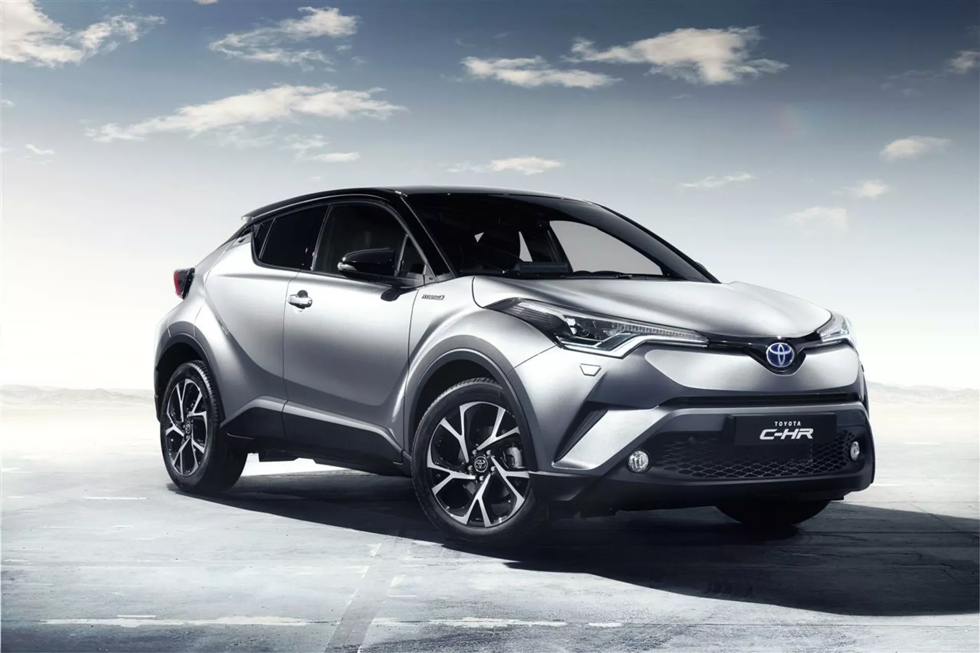 Srebrny Toyota C-HR 2016 w pozie trójkwartalnej przedniej prezentujący diody LED, koła ze stopów lekkich i elegancki design na komputerowo generowanym tle nieba, podkreślający sportowy i nowoczesny charakter.