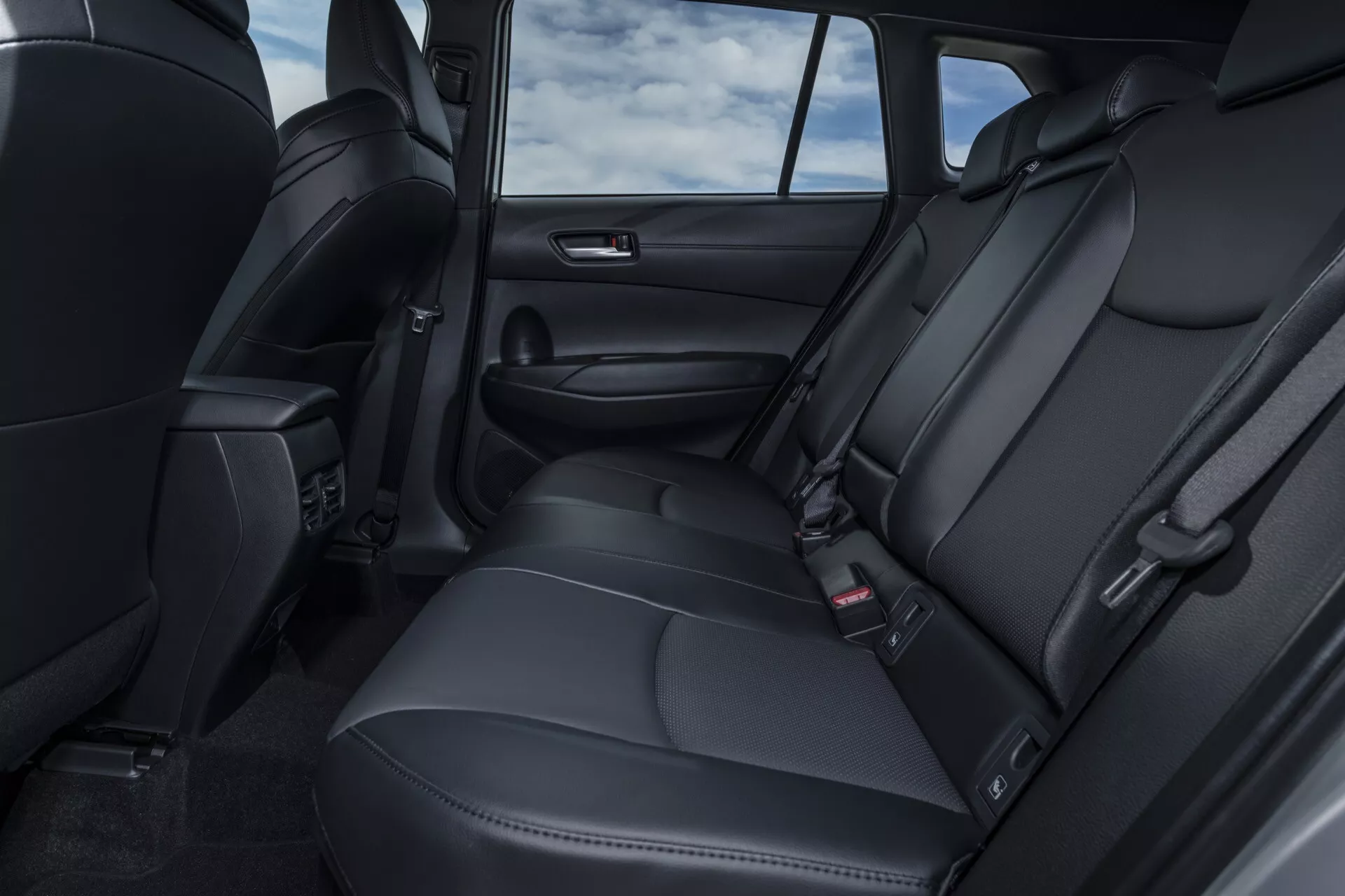 Widok tylnej kabiny Toyoty Corolla Cross 1. generacji 2022 z czarnymi skórzanych siedzeniami pasażerskimi z zagłówkami, nawiewami klimatyzacji i nowoczesnymi funkcjami technologicznymi