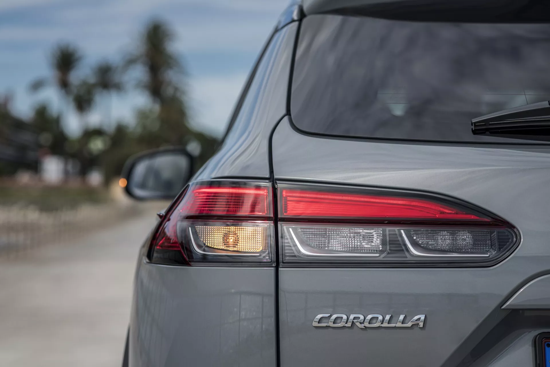 Zbliżenie na tylną prawą stronę Toyoty Corolla Cross 2022 z projektowaniem tylnych świateł LED, emblematem COROLLA, metalicznym szarym lakierem i zintegrowanym spojlerem w naturalnym otoczeniu