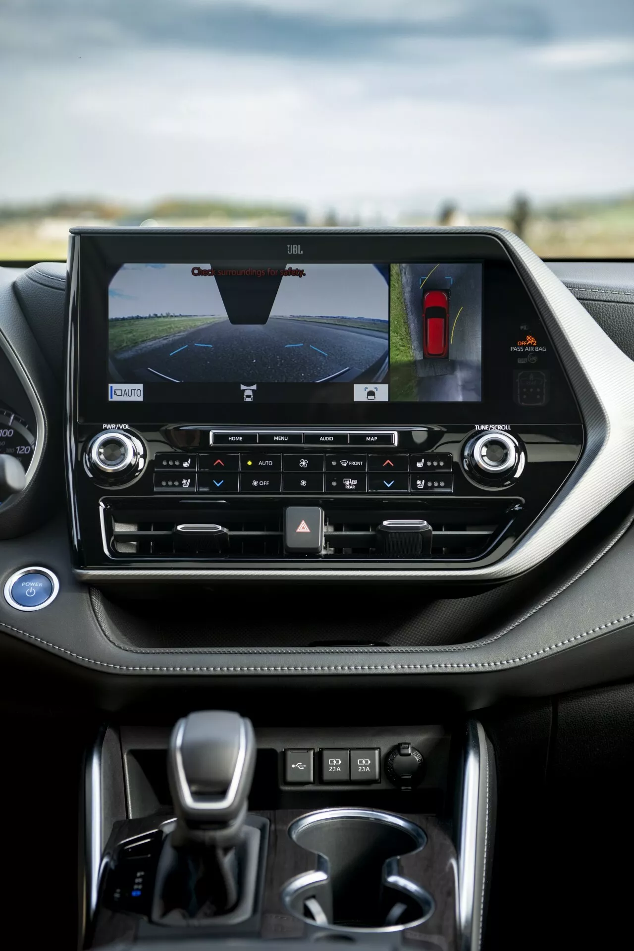 Wnętrze Toyoty Highlander 2021 z akcentem na konsolę środkową z poziomym ekranem dotykowym wyświetlającym kamerę cofania i asystenta parkowania, sterowanie klimatyzacją dwustrefową i dźwignię zmiany biegów automatycznej