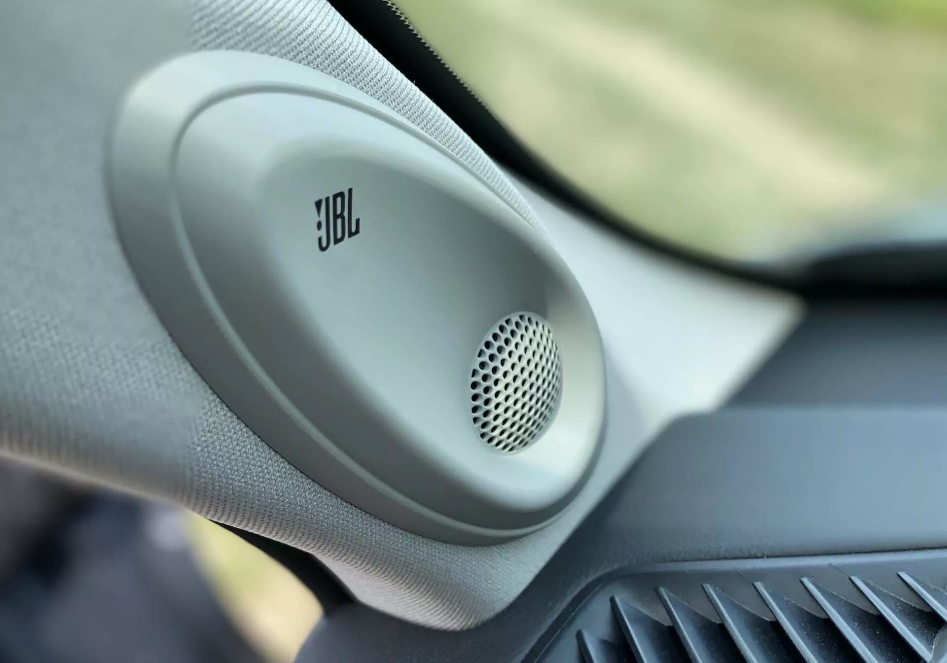 Zbliżenie wnętrza Toyota Highlander 2.5 Hybrid Business Edition 2021, z wyraźnym focusowaniem na głośnik JBL zamontowany w drzwiach z okrągłym grillem i teksturowaną obudową, podkreślającym wysokiej jakości audio samochodowe i cechy luksusowych pojazdów.