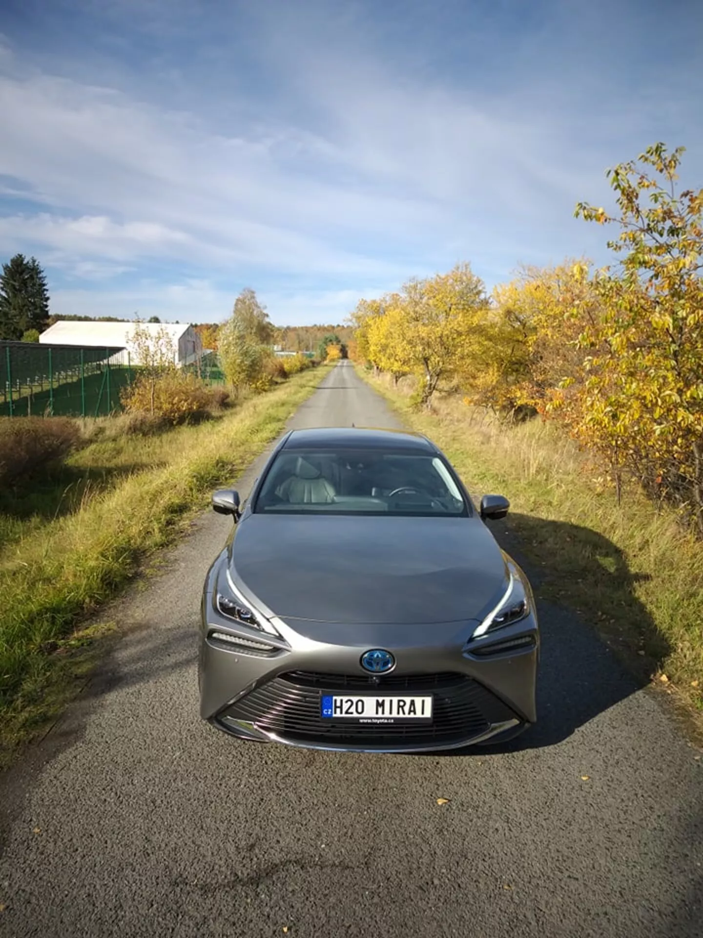 Toyota Mirai 2021 sfotografowana z przodu z lekko podwyższonego kąta, prezentująca jej smukłe reflektory LED i wyrazistą atrapę z centralnym emblematem, który może zawierać technologię sensorów, na tle półwiejskiego krajobrazu w naturalnym świetle dziennym, pokazująca zaawansowaną technologię ogniw paliwowych na wodór i aerodynamiczny design